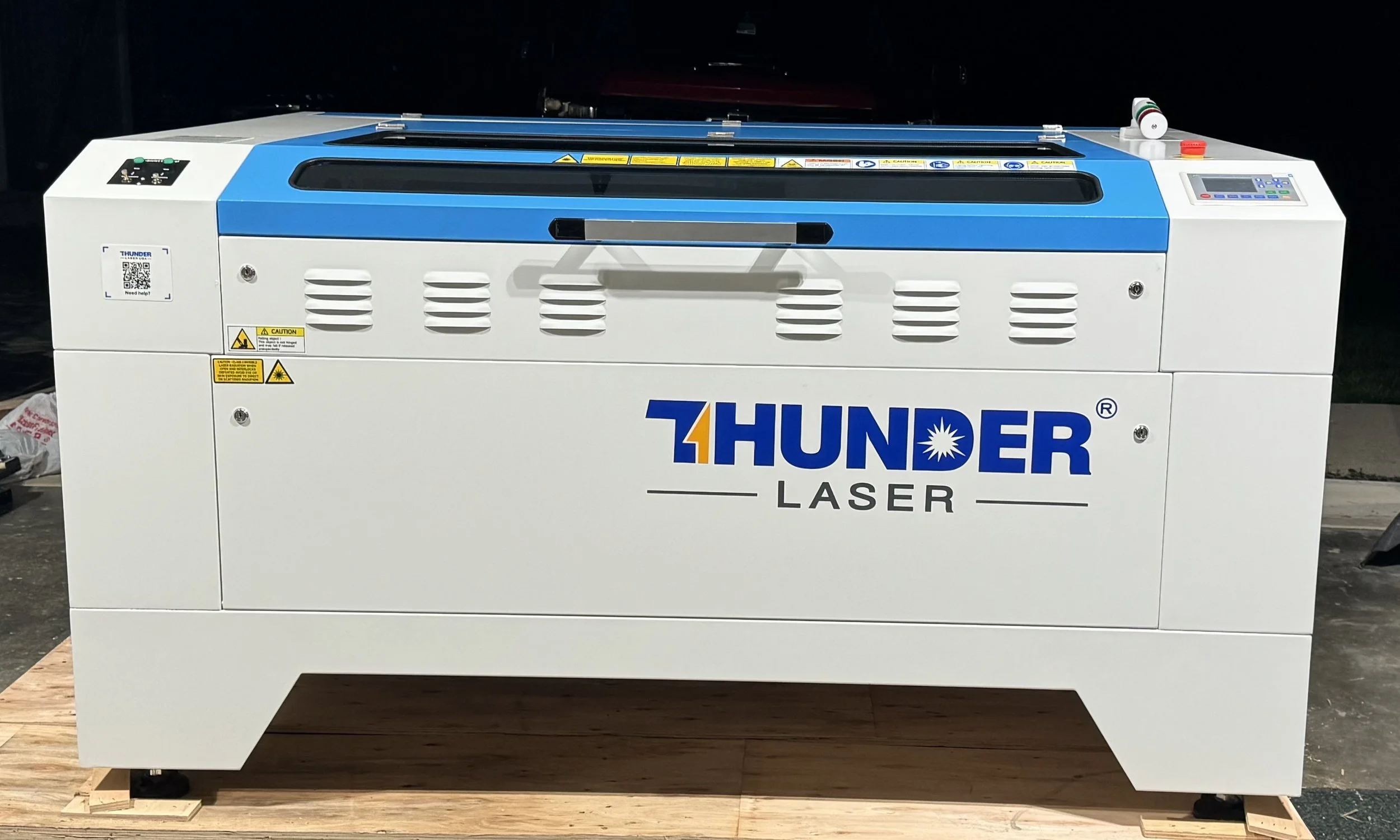 A large industrial laser cutting machine with the brand name 'Thunder Laser' printed on the front, featuring a blue top panel and control panel on the right side.