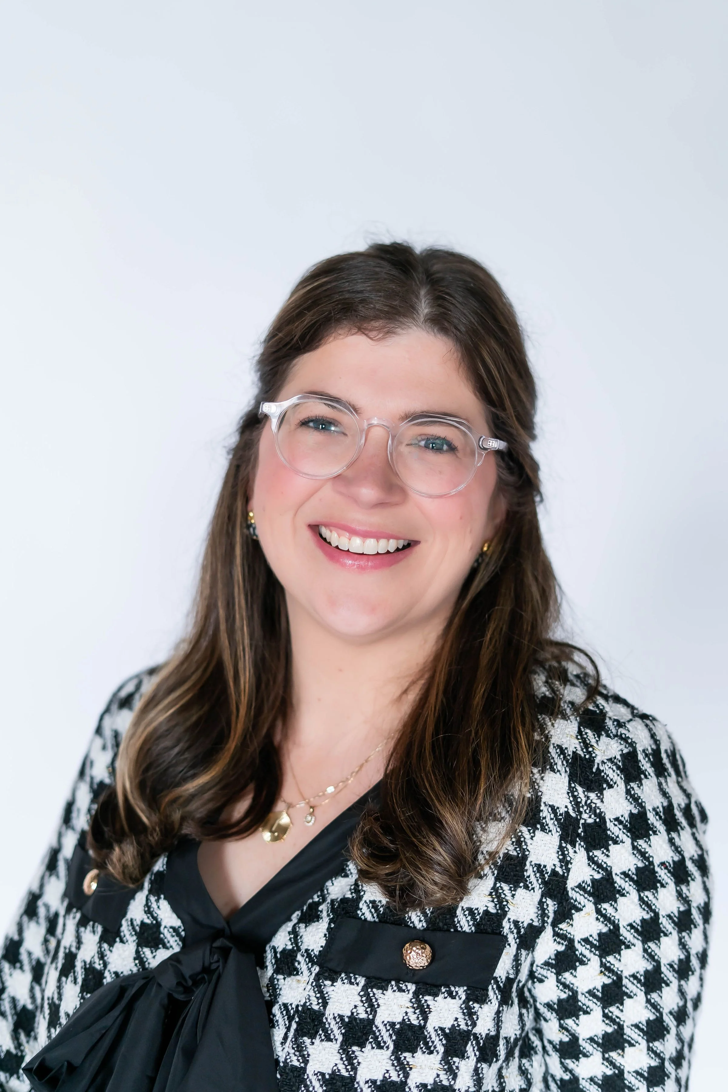 Portrait of a smiling woman with brown hair, glasses, and a black-and-white houndstooth blazer.