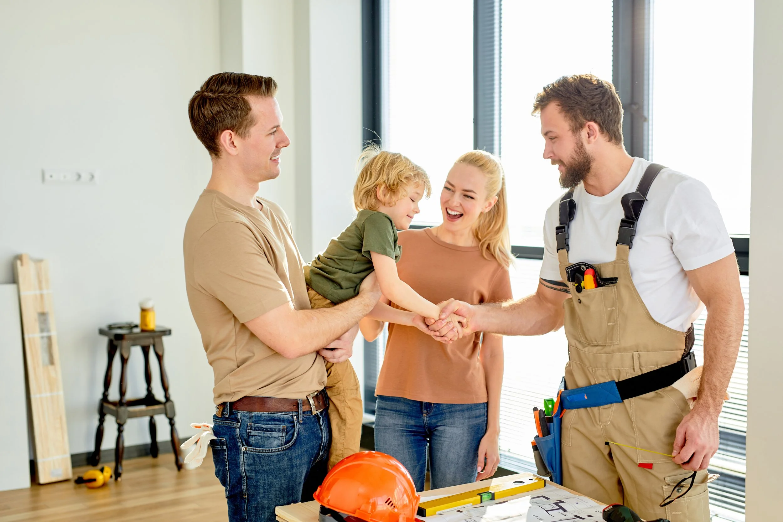 A young family lifts their toddler to meet a handyman performing repairs in their apartment.