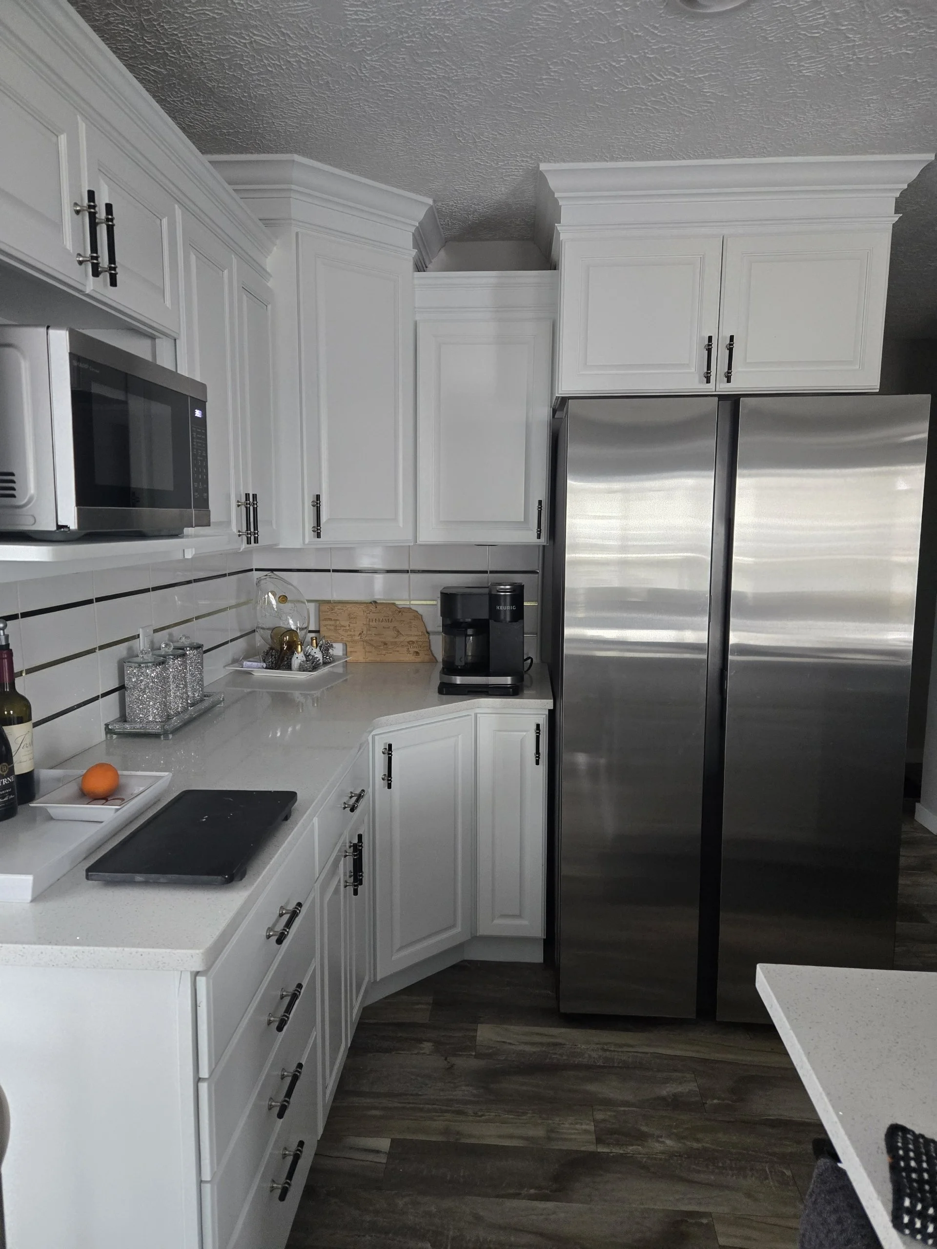 White kitchen with stainless steel refrigerator, microwave, coffee maker, and countertop with decorative items and an orange on a white tray.