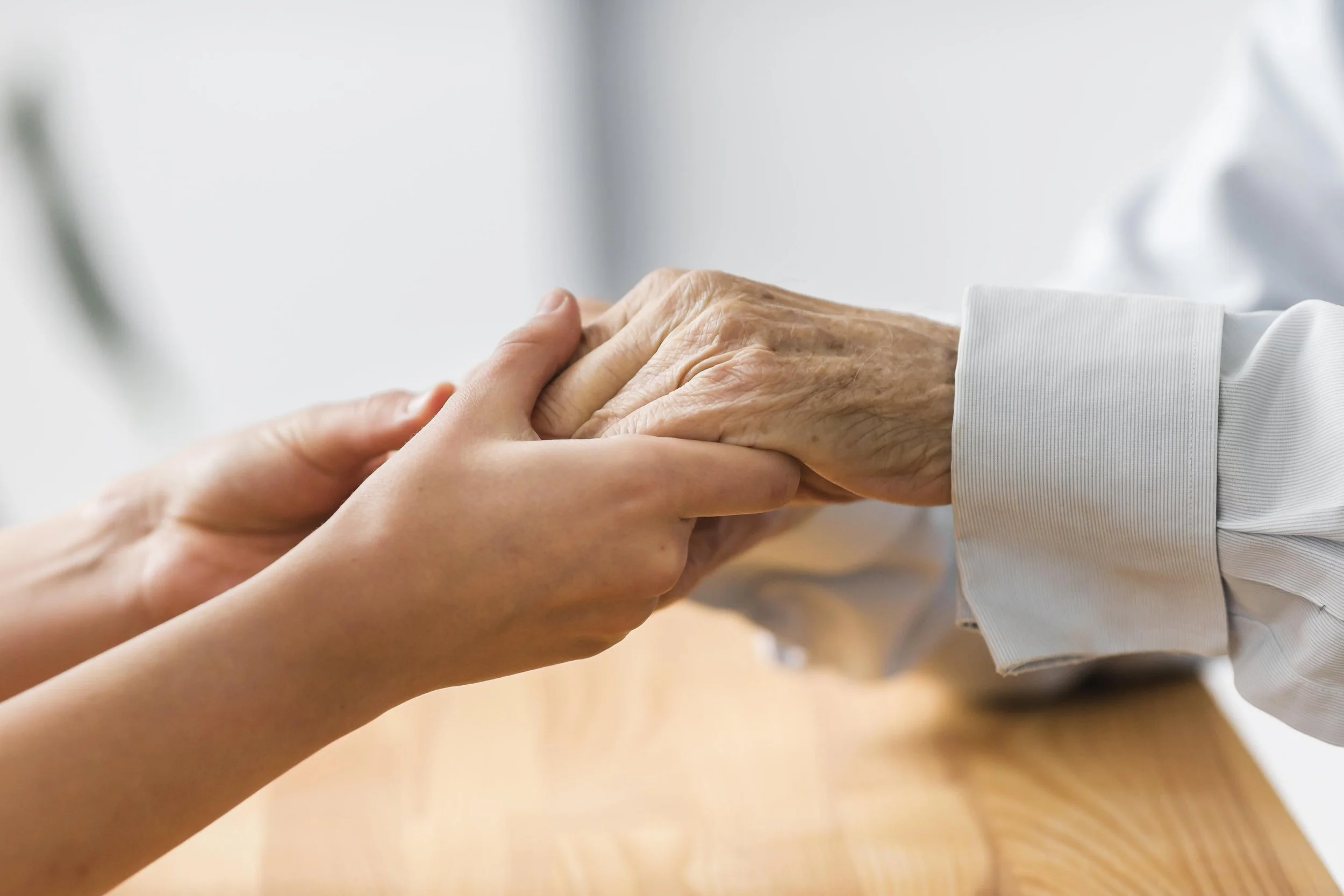 A young person holding the hand of an elderly person, gently supporting it.
