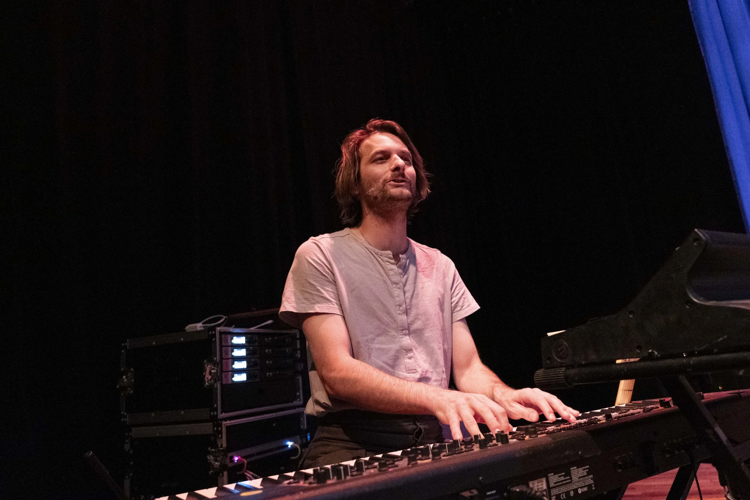 A man playing a keyboard on a stage with a black background.