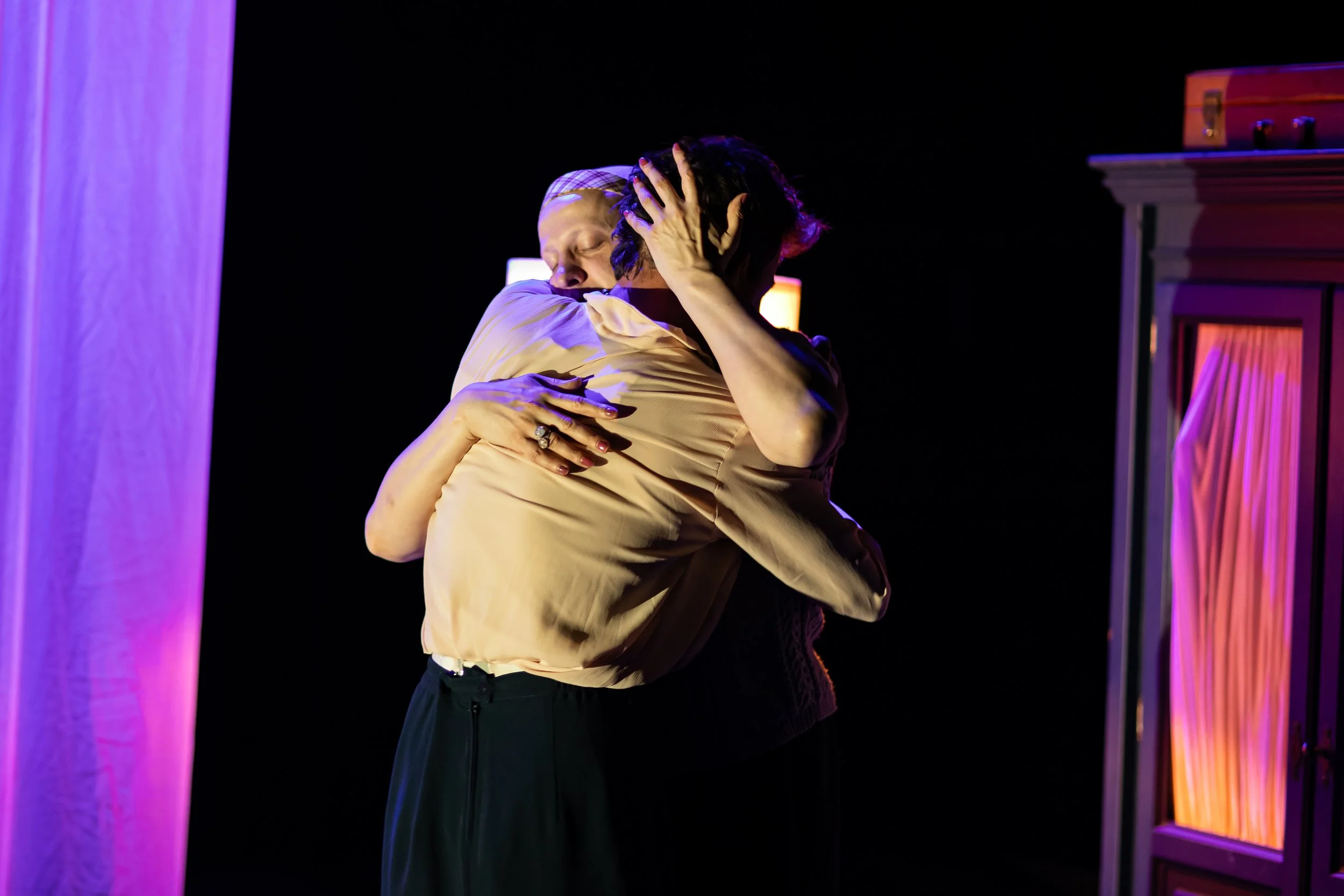 Two women embracing tightly on a stage with purple and orange lighting.