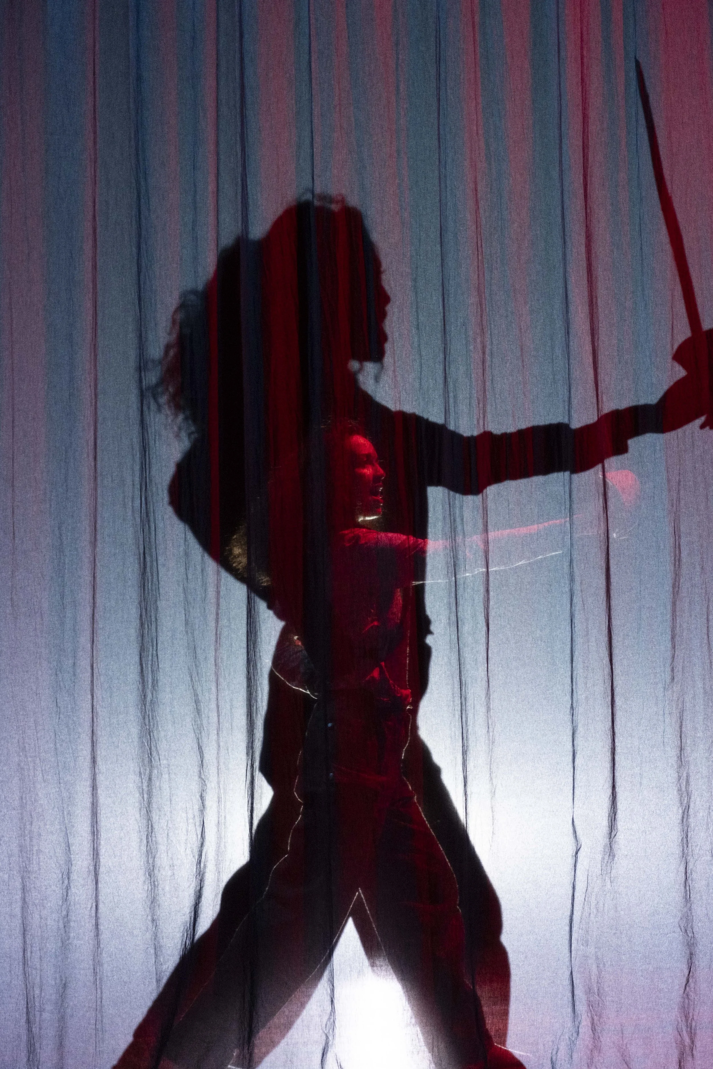 A silhouette of a woman holding an umbrella behind a semi-transparent curtain with vertical red and blue stripes.