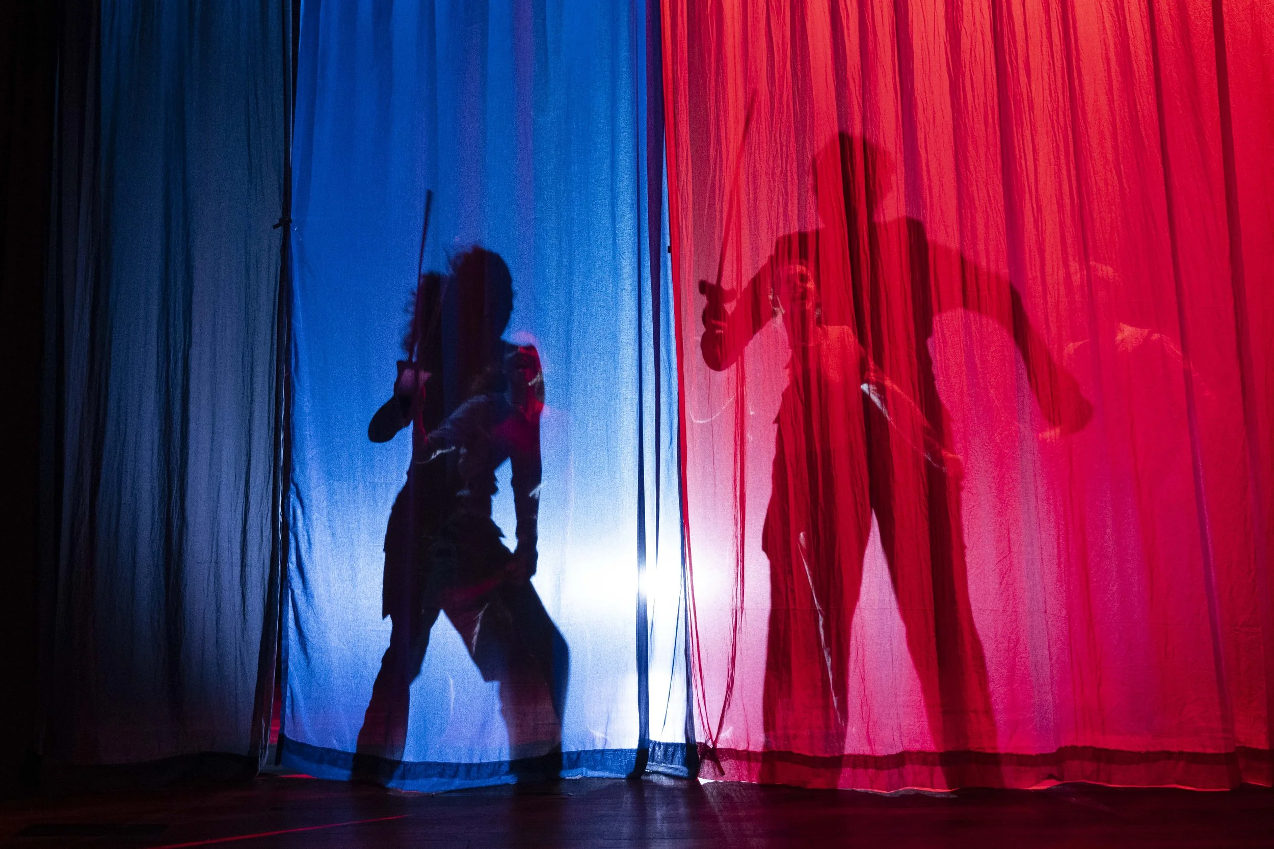 Shadow puppets of two people behind red and blue curtains, with one person holding a sword and the other a gun.