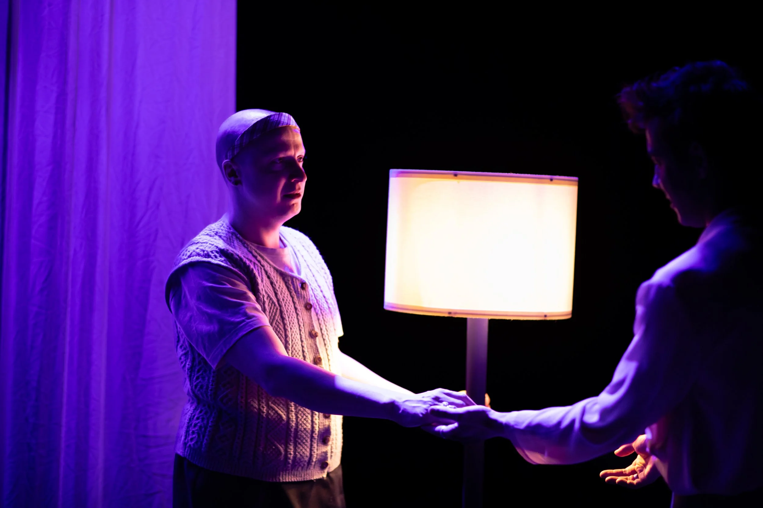 Two people holding hands in front of a lamp with purple and white lighting.