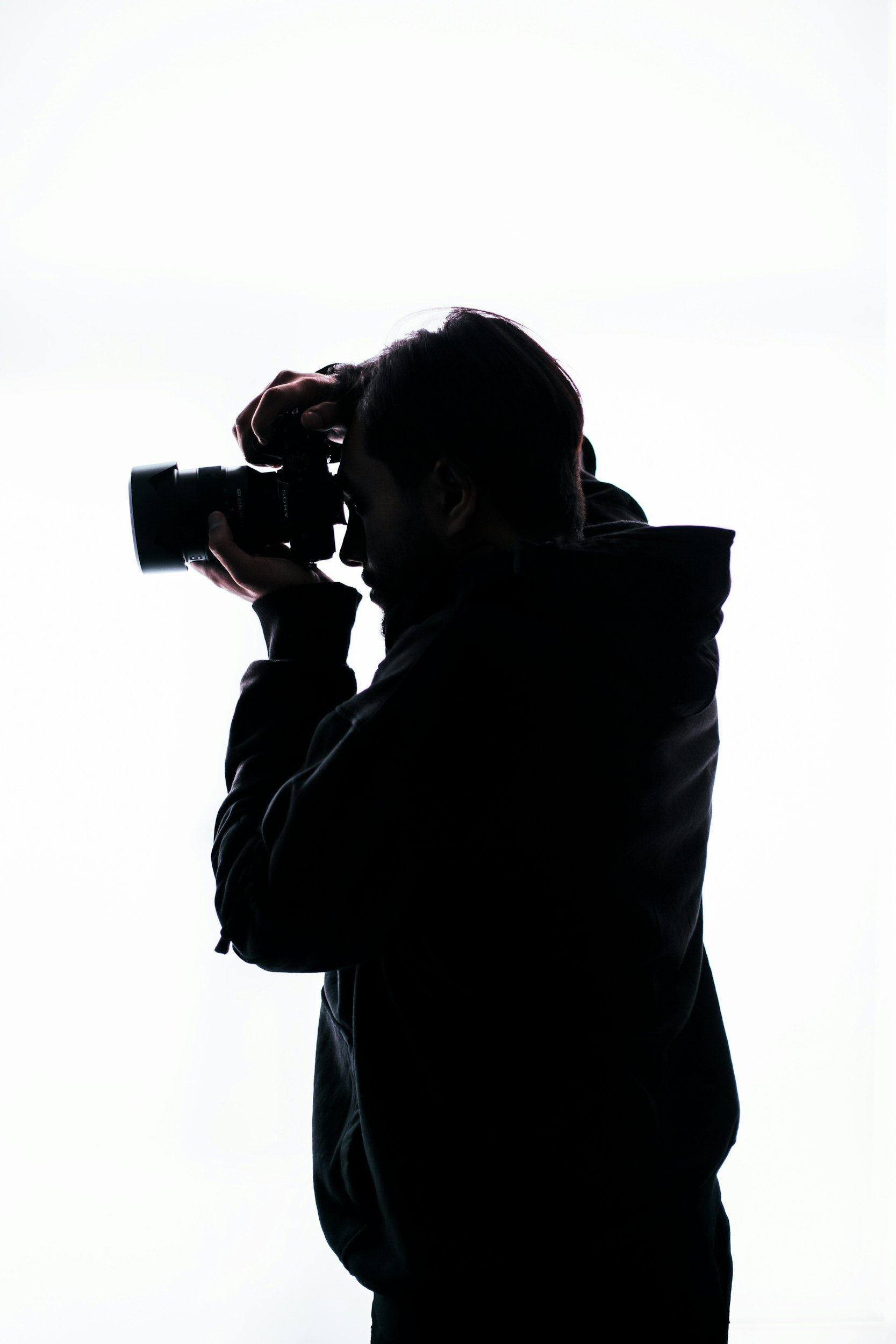 Silhouette of a person taking a photograph with a camera against a white background.