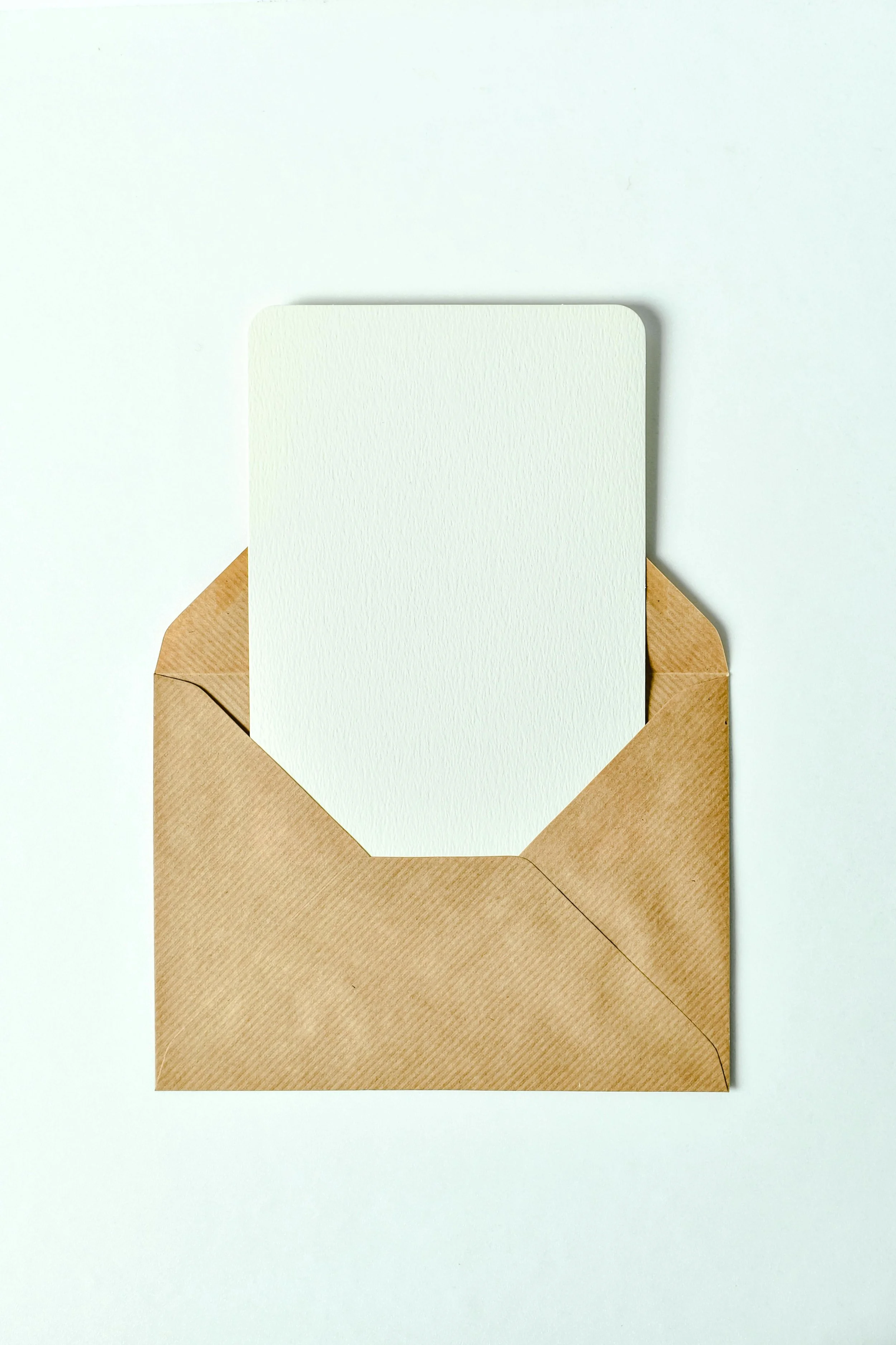 A blank white card in a brown paper envelope on a white surface.