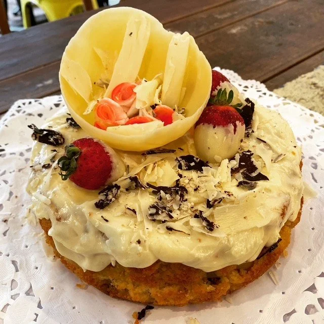 Decorative cake with white frosting, strawberries, chocolate shavings, and white chocolate curl on top, on a lace doily.