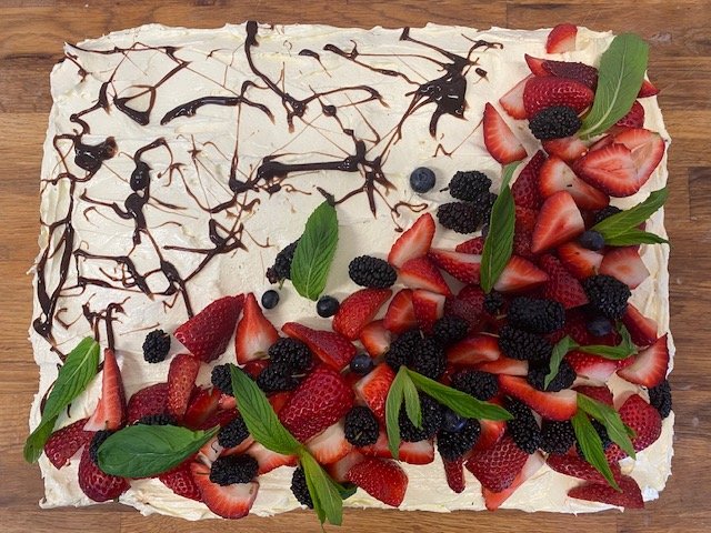 A rectangular fruit tart topped with sliced strawberries, blackberries, blueberries, fresh mint leaves, and drizzled with chocolate.