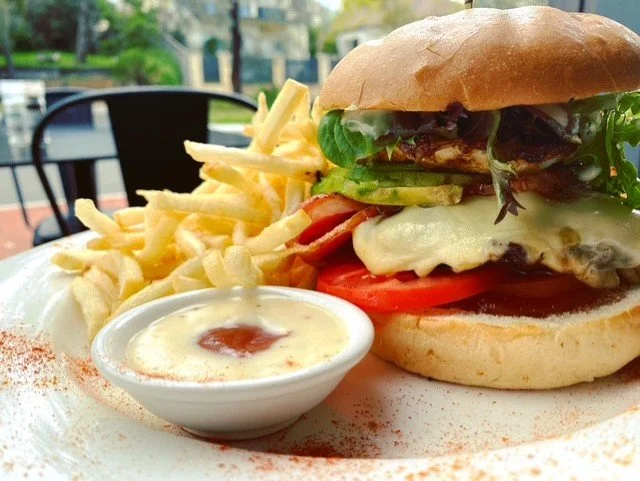 Burger with lettuce, tomato, cheese, and a meat patty in a bun, served with French fries and a small bowl of dipping sauce on a plate.