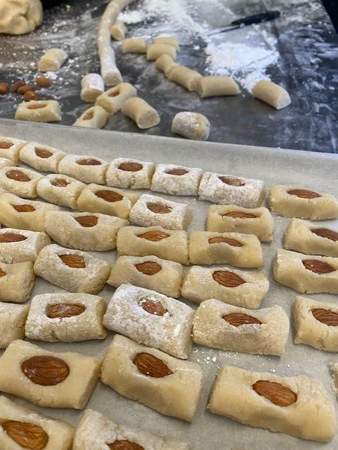Unbaked almond-filled cookies on a baking sheet, with dough pieces and flour in the background.