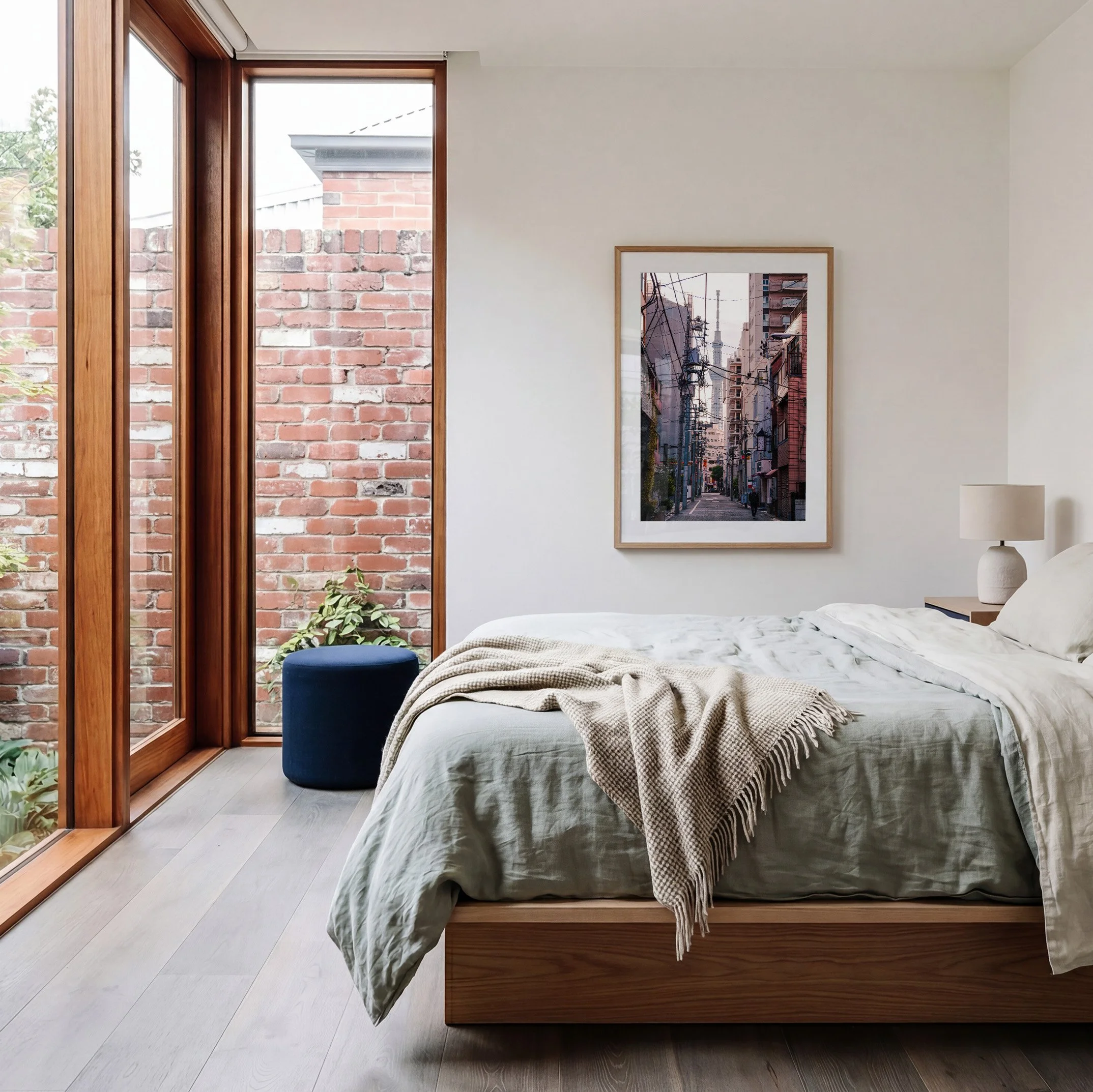 Tokyo Skytree photography print displayed in an oak frame in a bright contemporary bedroom with exposed brick and blue ottoman.