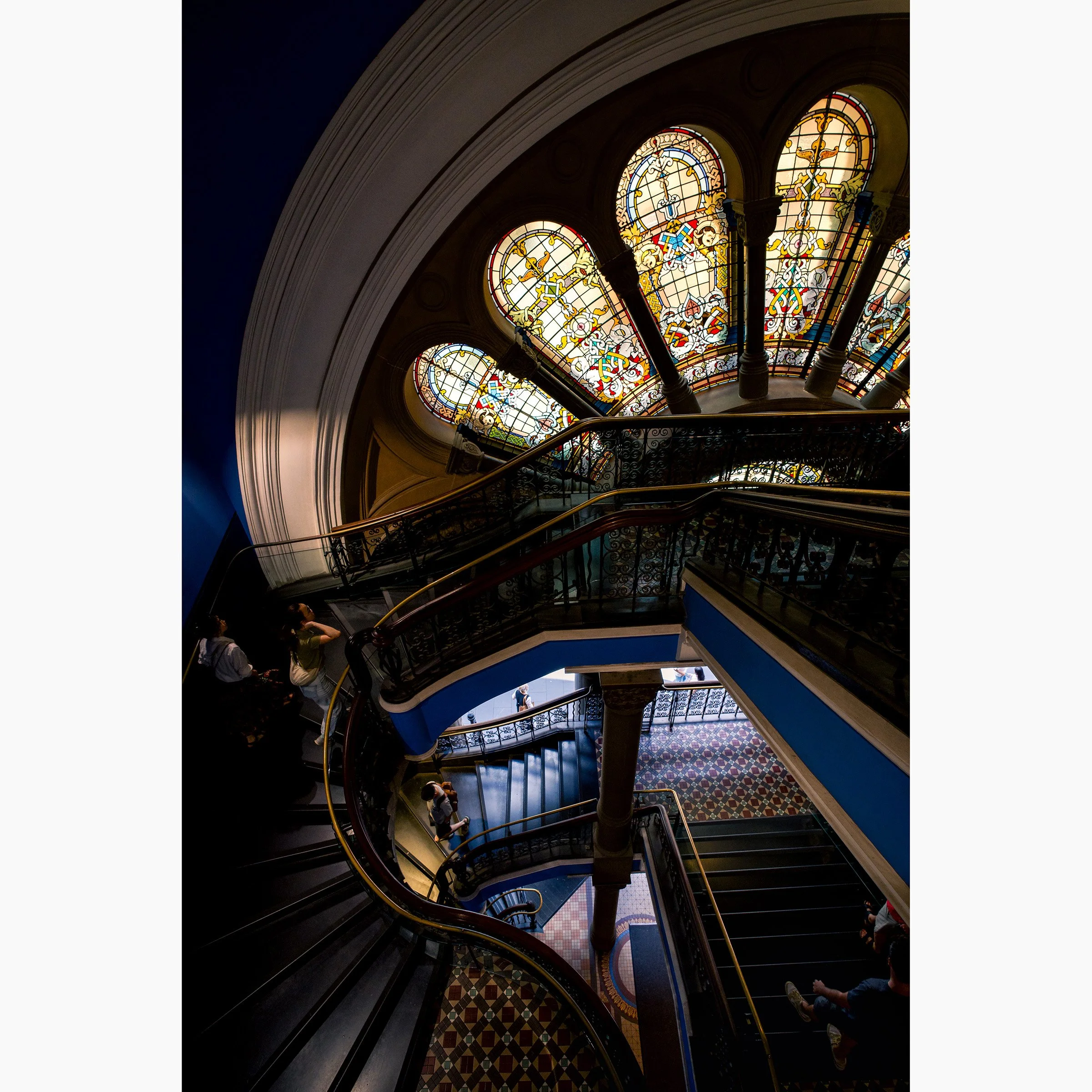 Stained glass windows and curved staircases inside Sydney's Queen Victoria Building captured in a dramatic architectural photograph.