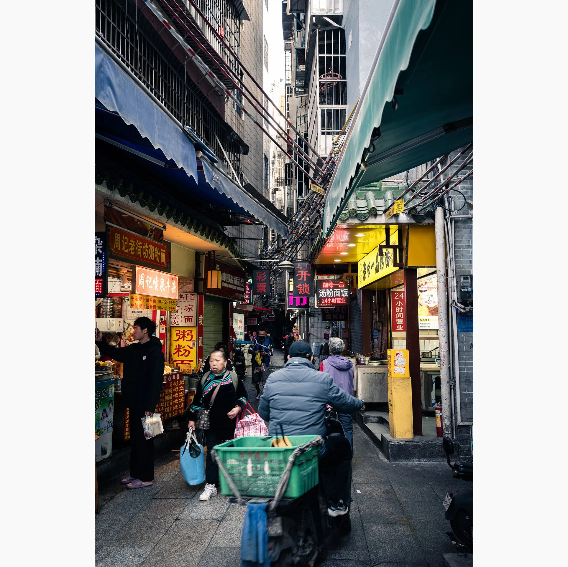 Busy Guangzhou alley lined with food stalls, neon signs, overhead cables and pedestrians, capturing the energy and character of everyday street life in China.