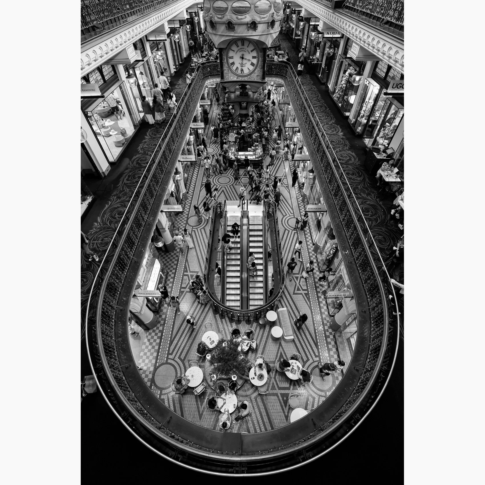 Black and white overhead view inside Sydney's Queen Victoria Building, capturing the central clock, escalators, shoppers and ornate architectural details.