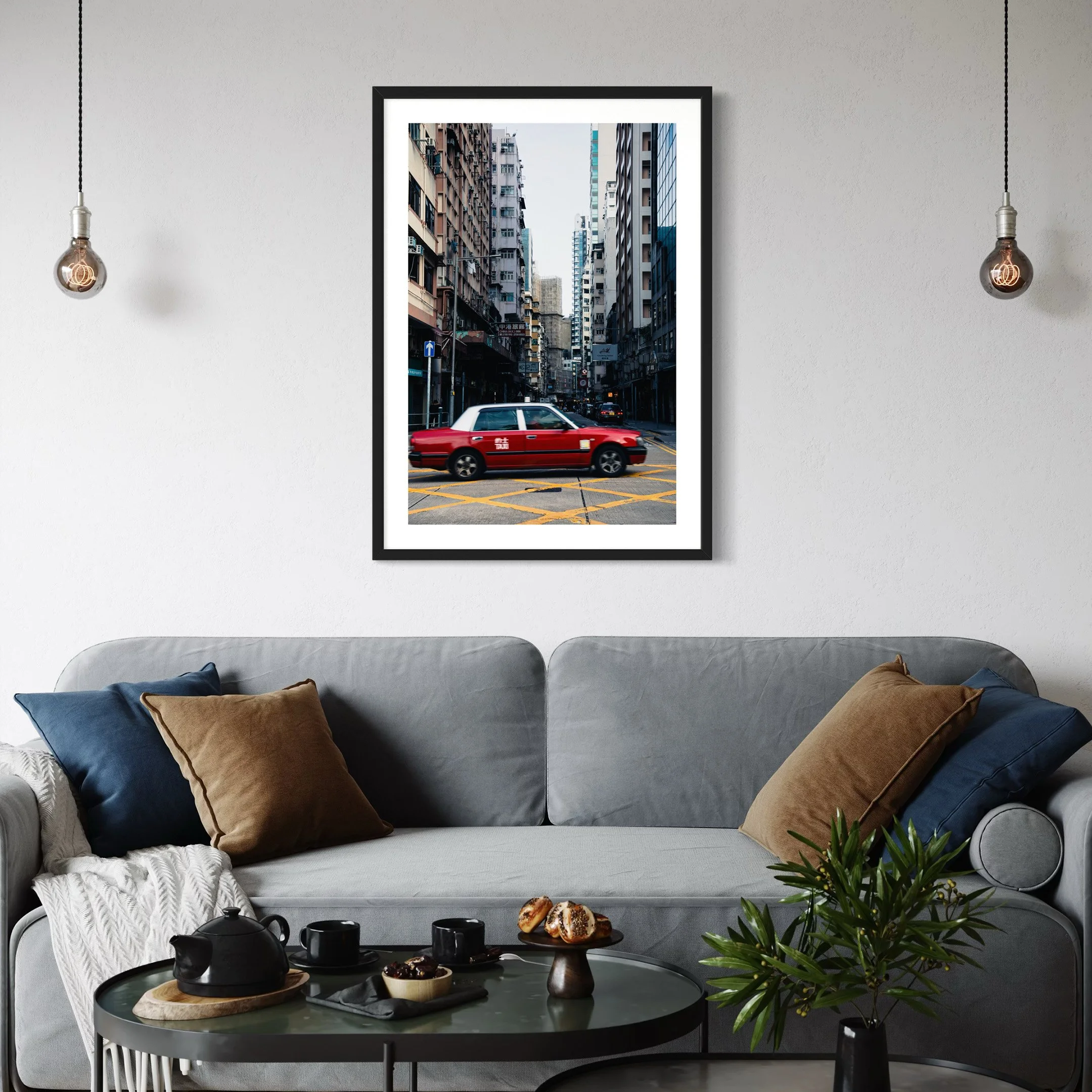 Vertical Hong Kong city print with a red taxi displayed above a grey couch in a contemporary living room setting.