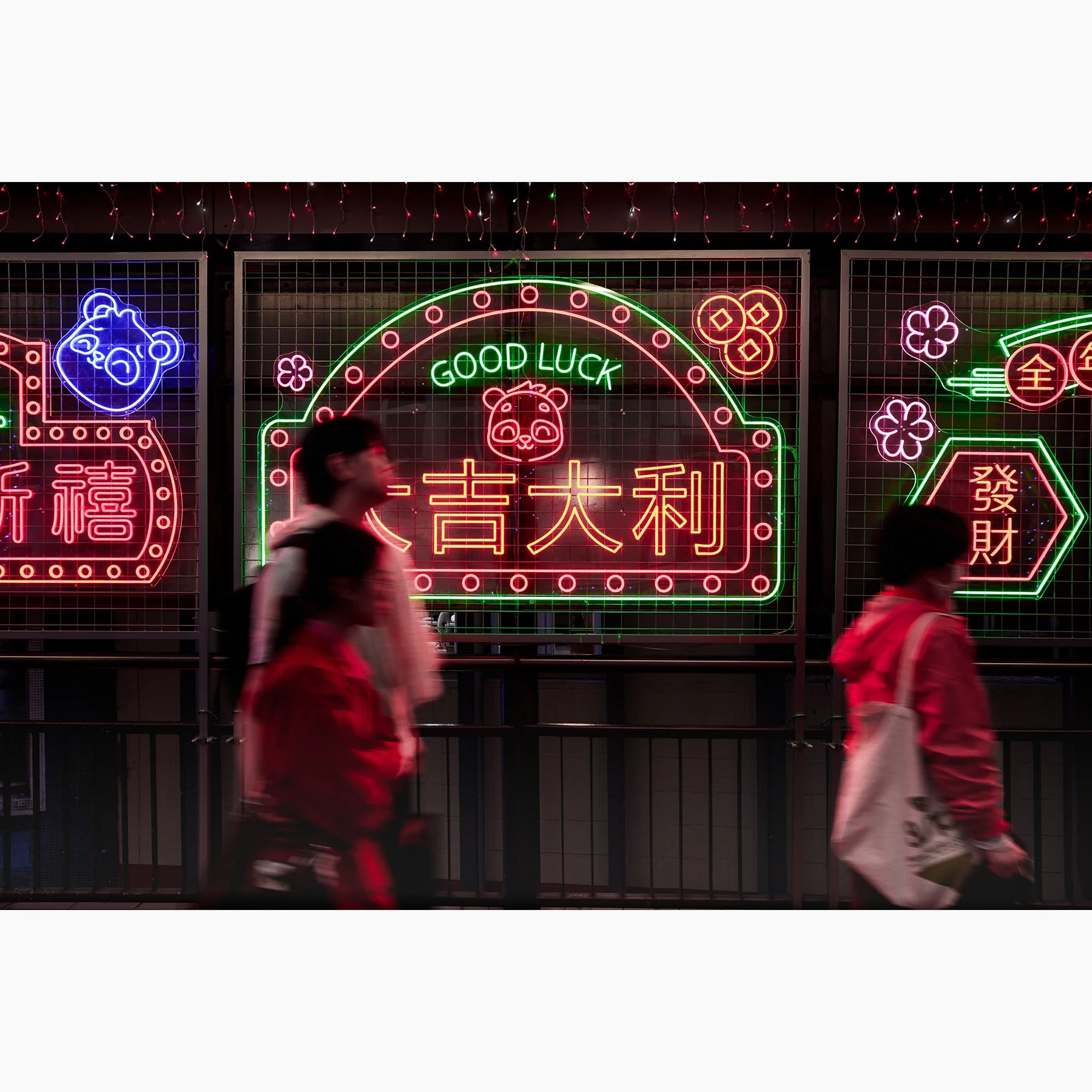 Hong Kong neon street photography print featuring pedestrians walking past a bright GOOD LUCK sign with colourful Chinese characters and glowing city lights at night.