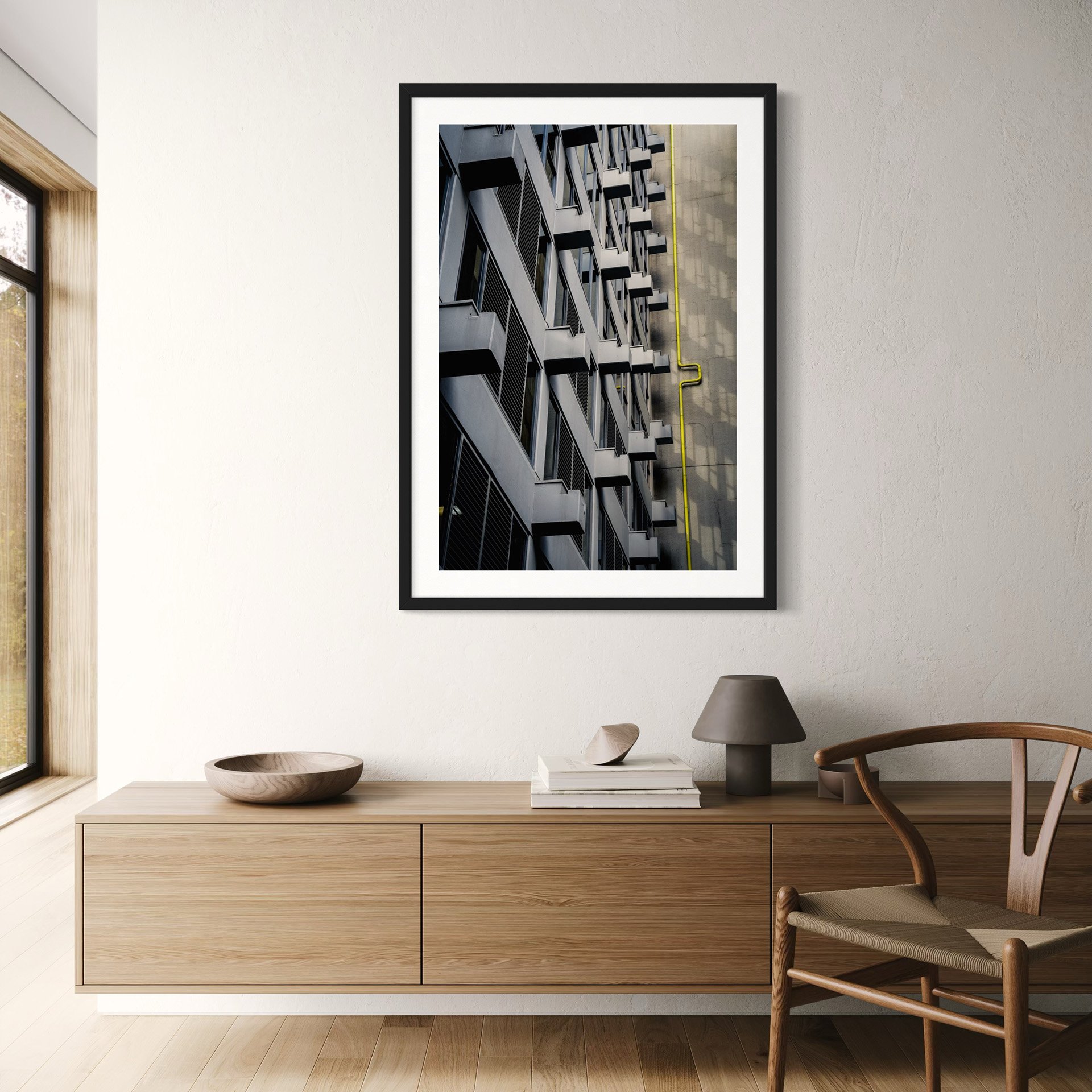 Contemporary living room featuring a framed architectural photograph of a grey building façade with a striking yellow pipe above a light timber sideboard.