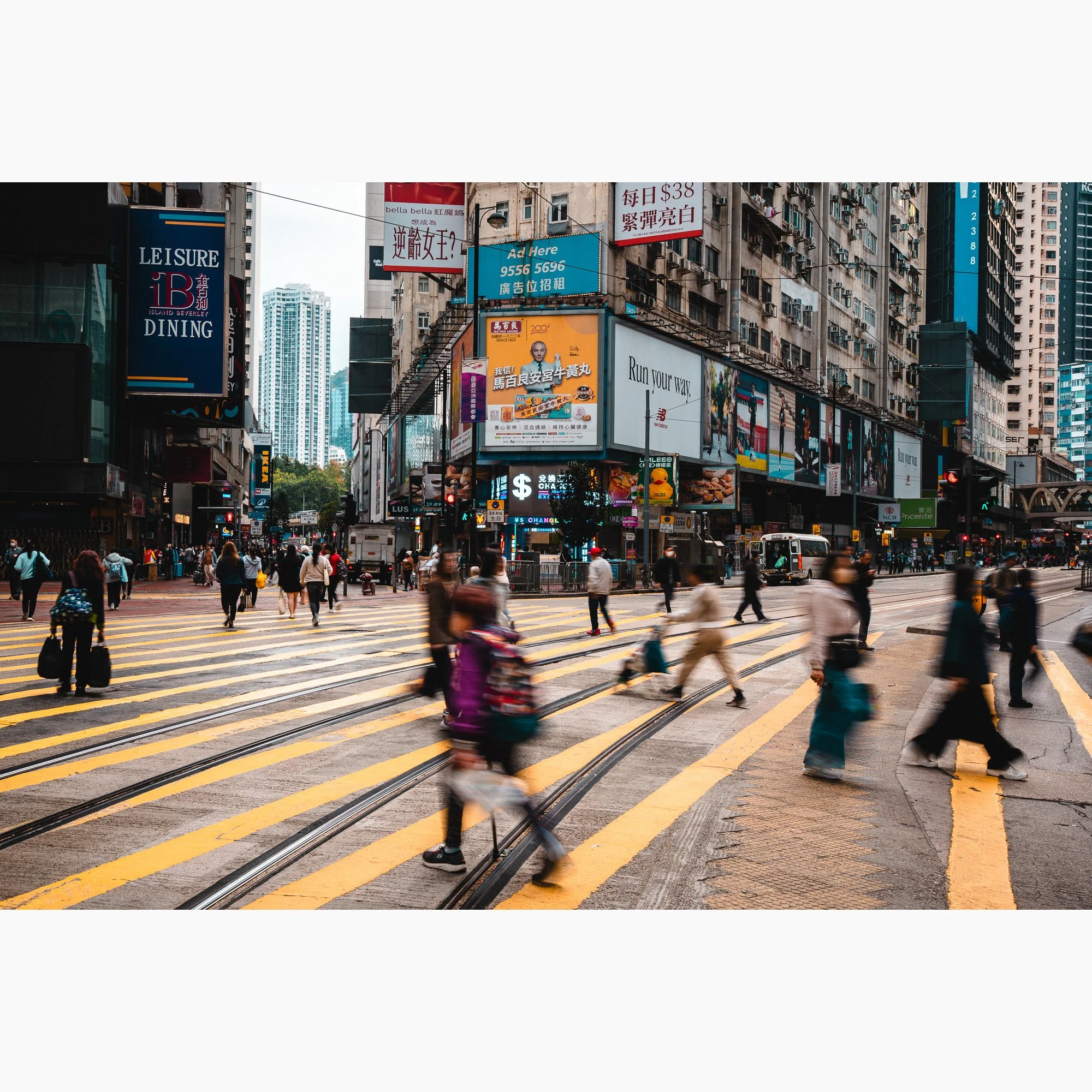 Hong Kong city street scene featuring blurred pedestrian movement, tram tracks, dense signage and layered urban architecture.