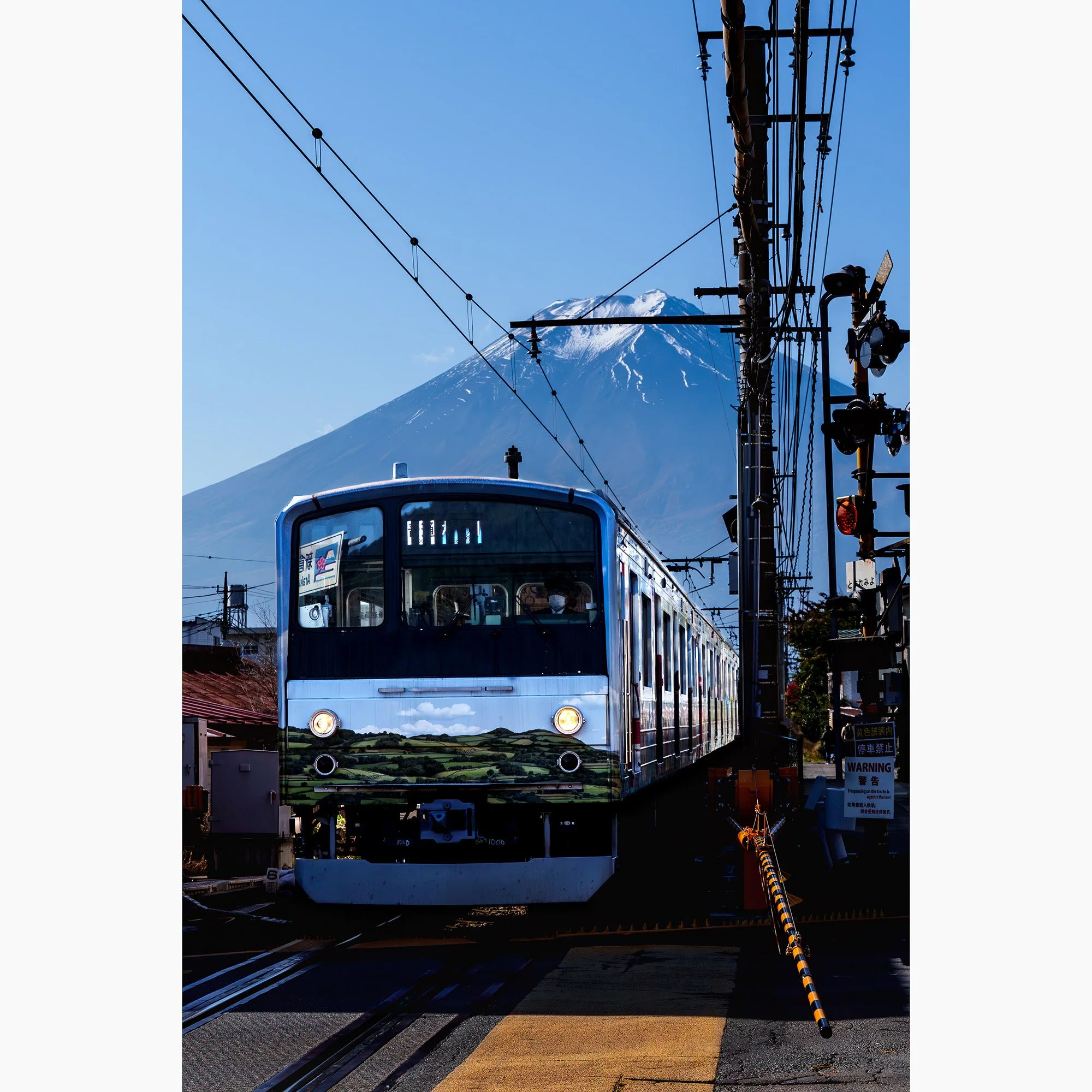 Train passing beneath Mount Fuji in Japan with overhead railway lines