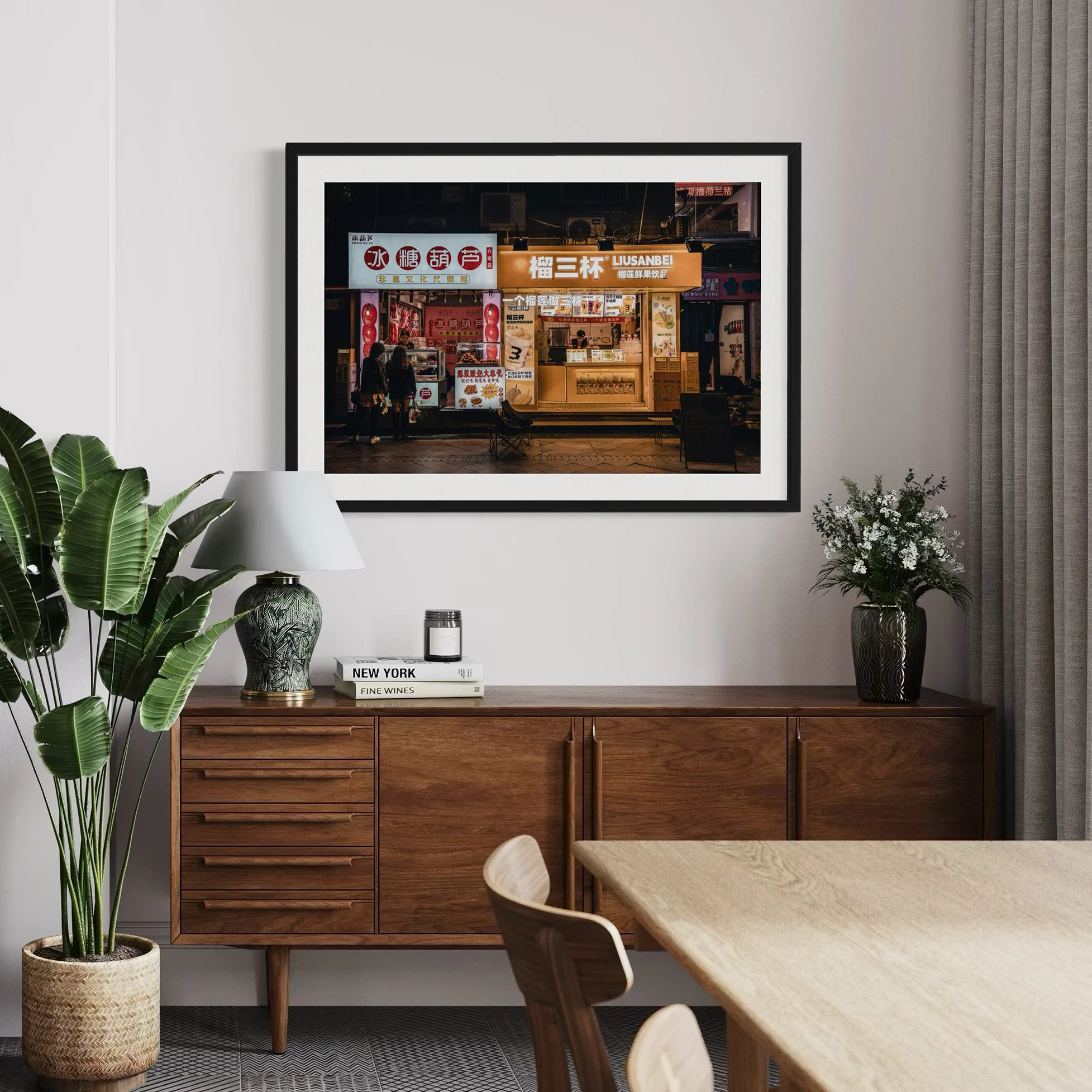 Framed Guangzhou street photography print displayed above a wooden sideboard in a modern dining interior with warm neutral tones and indoor plants.
