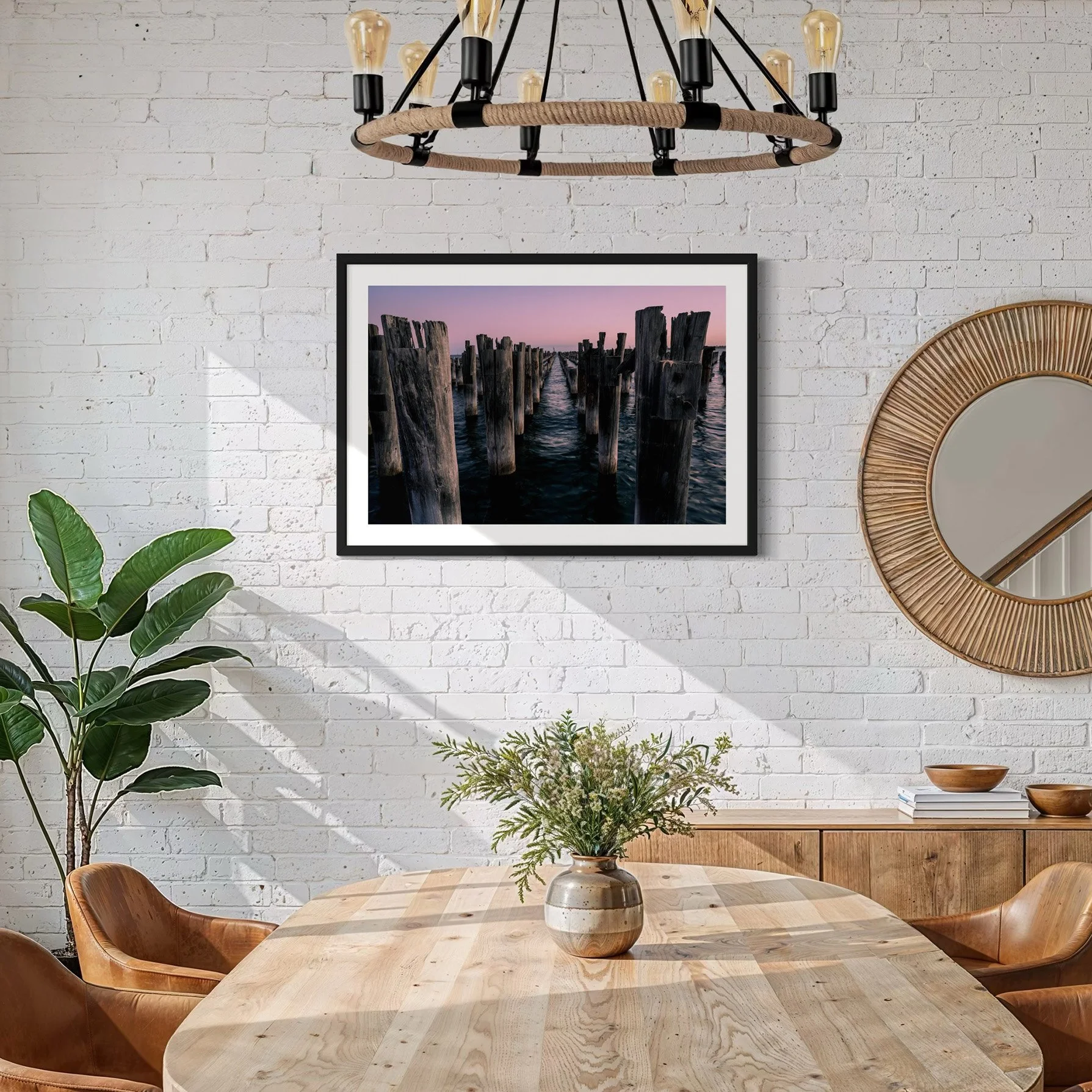 Large framed Melbourne coastal photography print featuring Princes Pier timber pylons displayed in a bright dining room with white brick walls and natural timber furnishings.