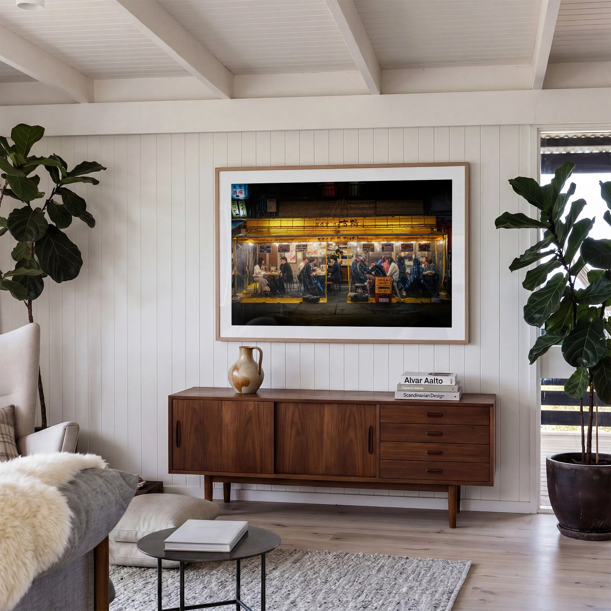 Tokyo night street photography print in a natural oak frame above a timber sideboard, in a bright living room with white panelled walls and indoor plants.