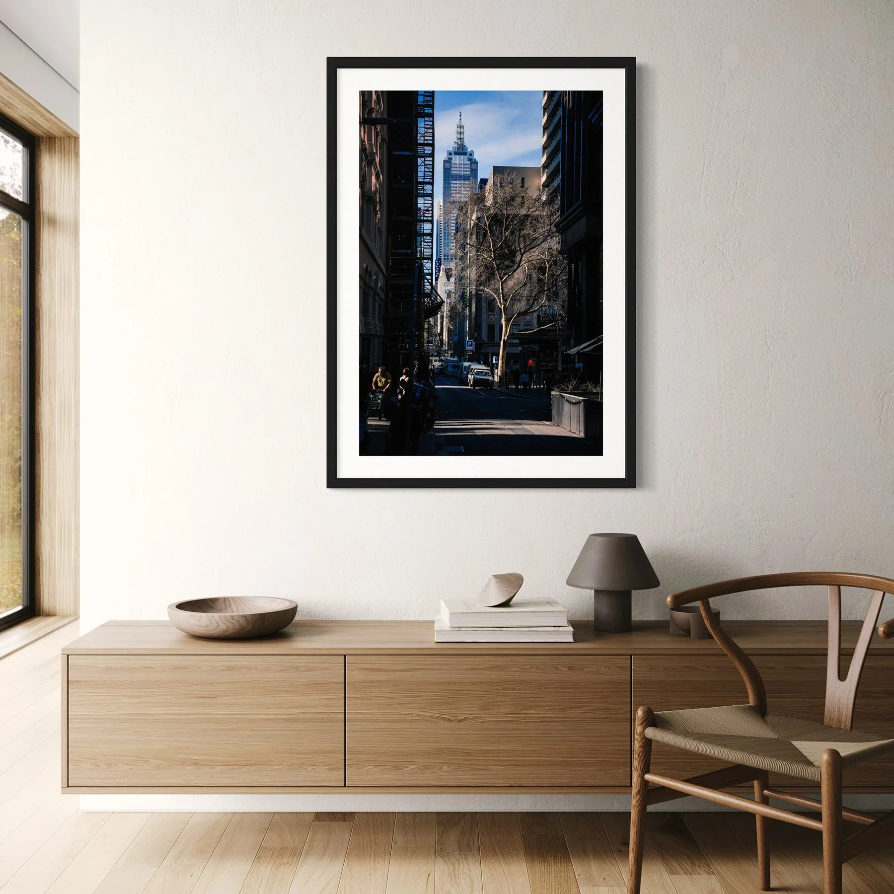 Framed Melbourne city photography print displayed above a light oak floating sideboard in a contemporary living space.