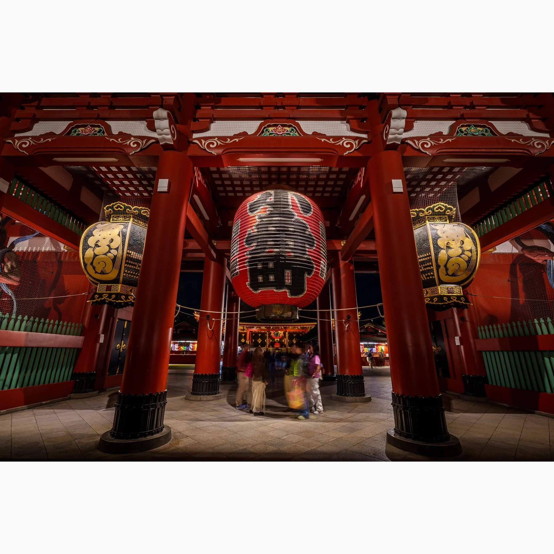Night photograph of Senso-ji temple in Tokyo, Japan, with its giant red lantern, red columns and moving visitors.