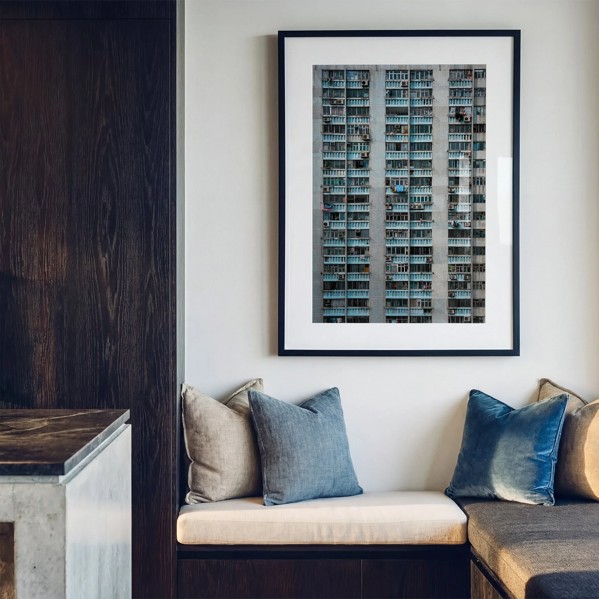 Hong Kong architecture photography print displayed in a black frame with white mat above a built-in window seat with blue cushions.