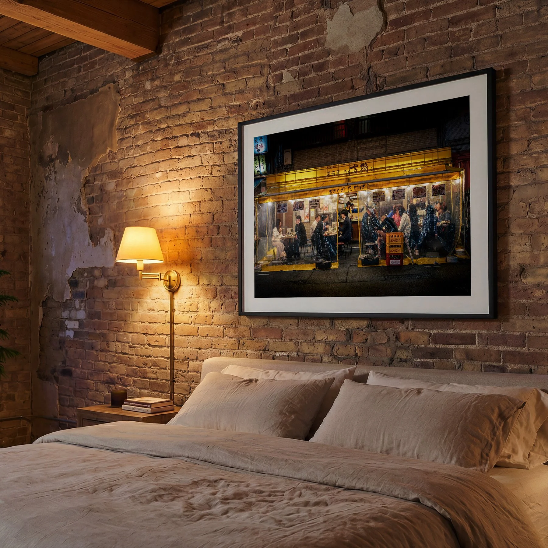 Framed Tokyo izakaya photography print displayed above a bed against an exposed brick wall, with warm bedside lighting and neutral bedding.