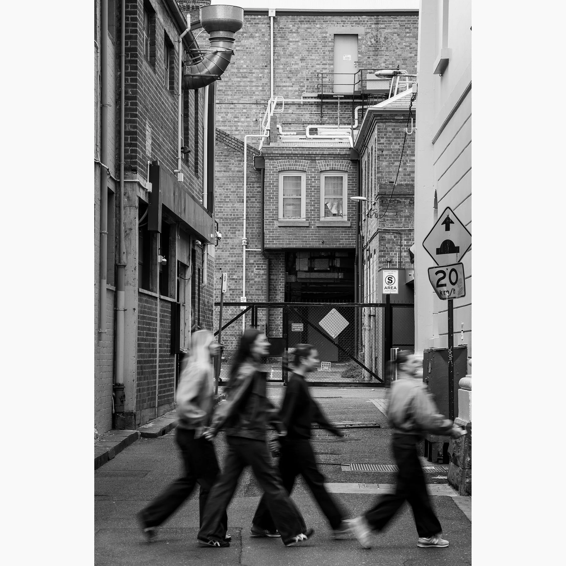 Black and white Melbourne laneway photograph featuring motion-blurred pedestrians, brick buildings and layered urban architecture.
