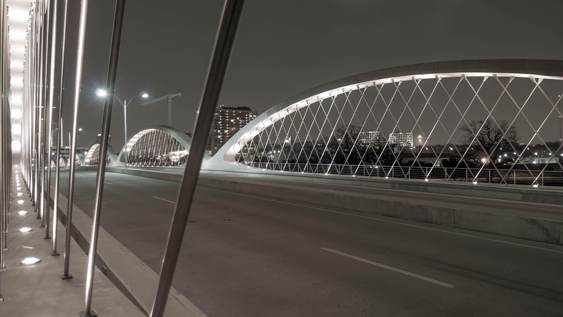 Empty bridge at night with lit arches and city skyline in the background.