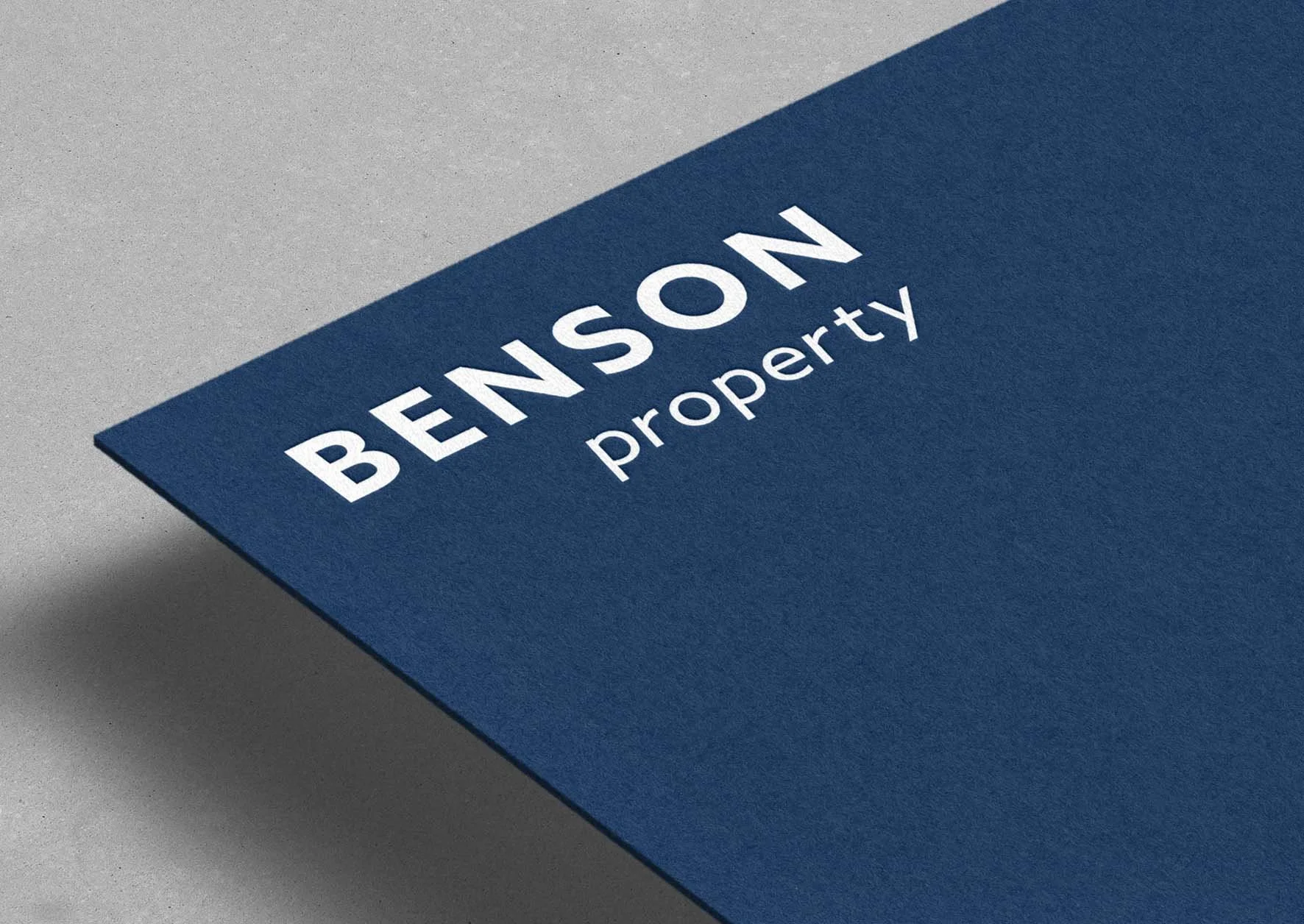 Close-up of a blue business card with white text that reads 'BENSON Property' on a grey surface.