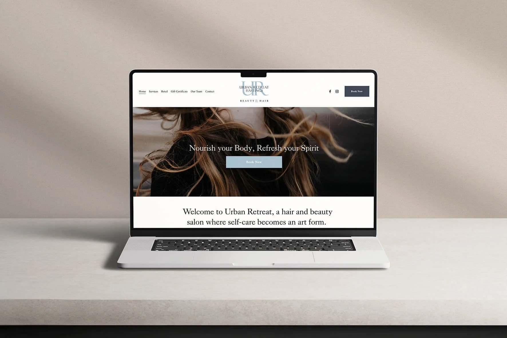 A silver laptop on a beige surface displaying the homepage of Urban Retreat Hastings, a hair and beauty salon website, with a background image of a woman with long flowing hair and a welcoming message.