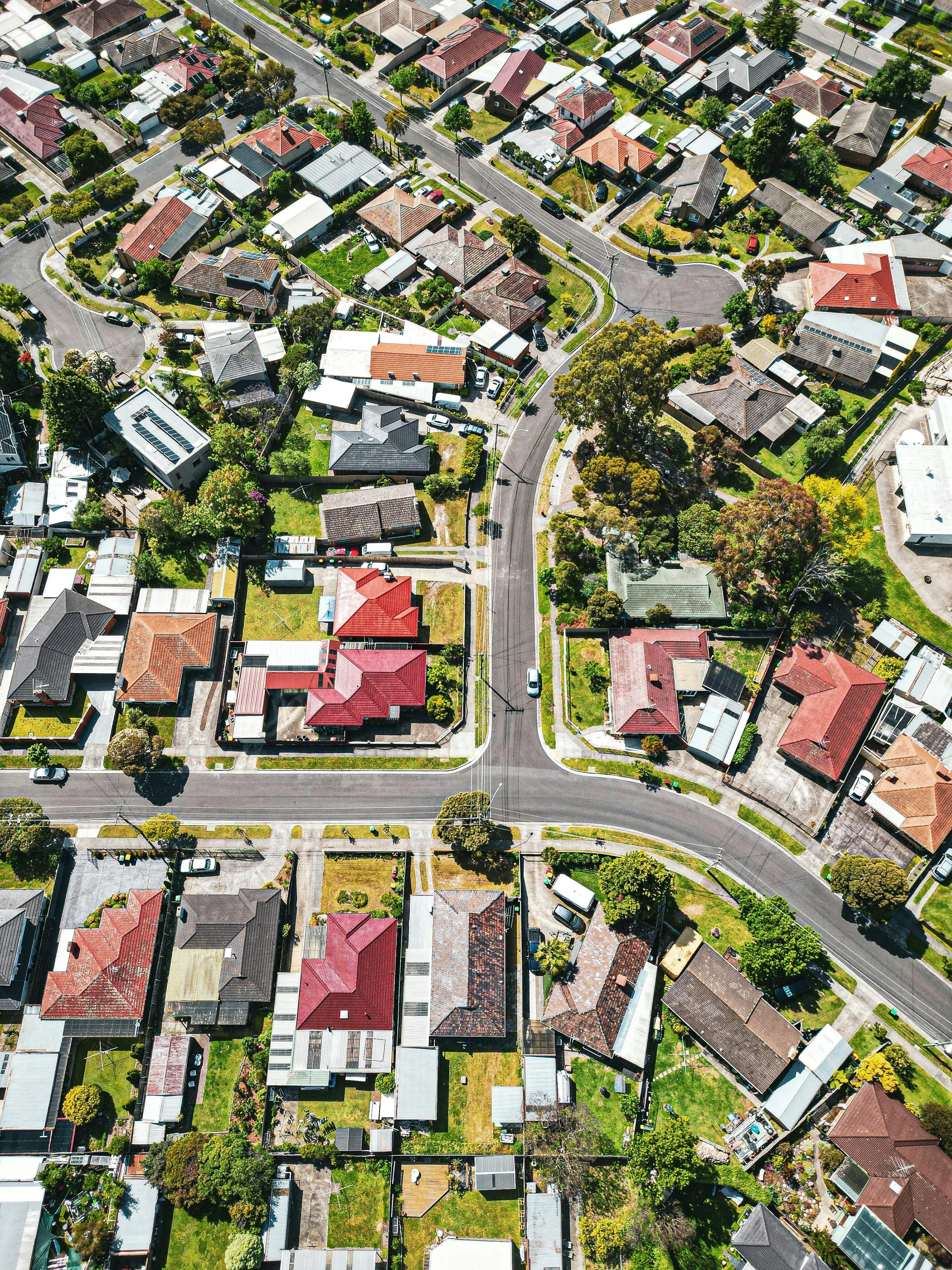 An aerial view of a suburban neighborhood with numerous houses, trees, lawns, and streets.