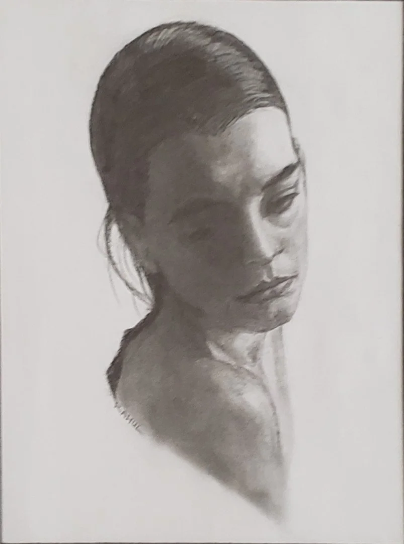 A black and white portrait of a woman with her head turned slightly to the side, with her hair pulled back, showing her face and shoulder.