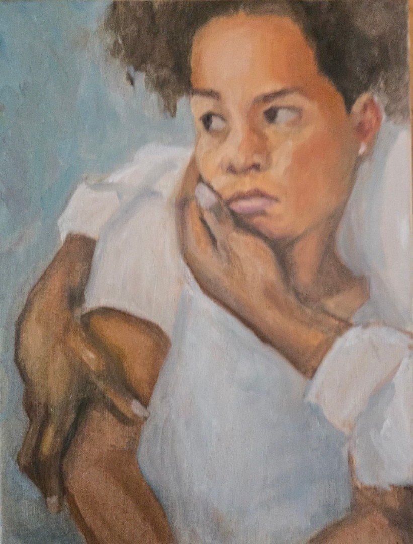 Portrait of a woman with short curly hair, resting her chin on her hand, wearing a white shirt, against a muted blue background.