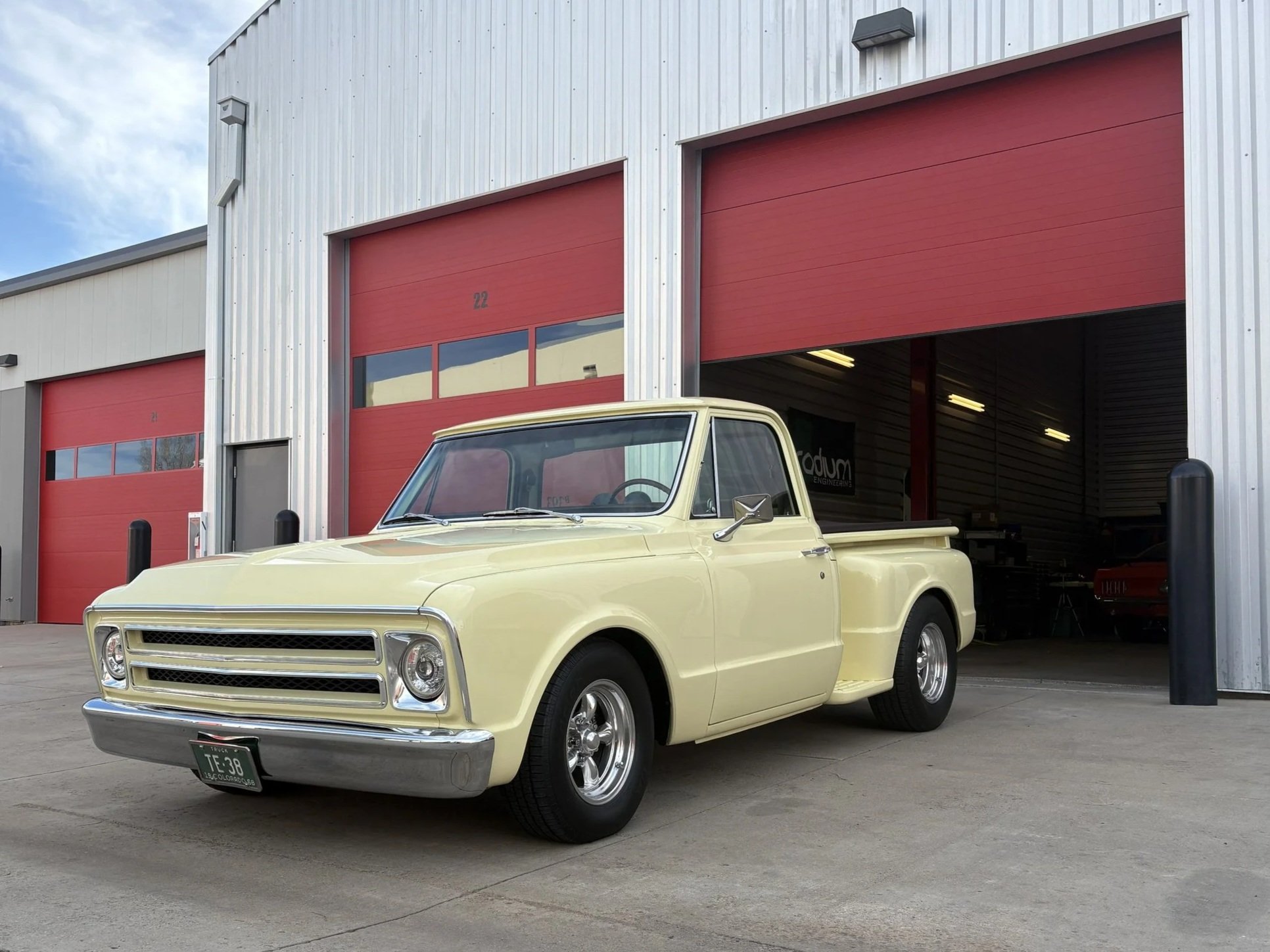 A vintage cream-colored pickup truck parked outside a building with red garage doors.