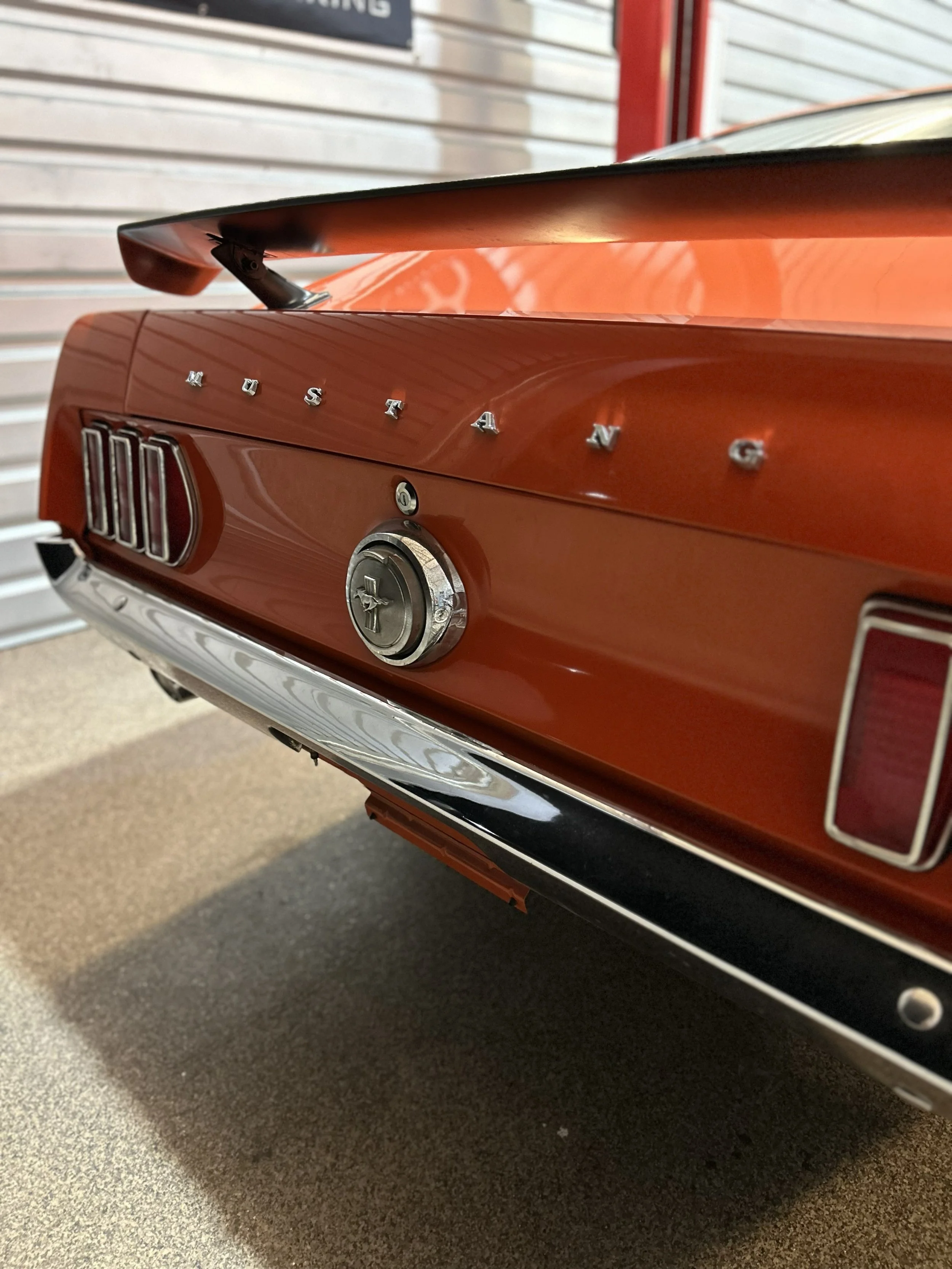 Close-up of the rear of a vintage orange Ford Mustang showcasing the emblem, taillights, and trunk lid.