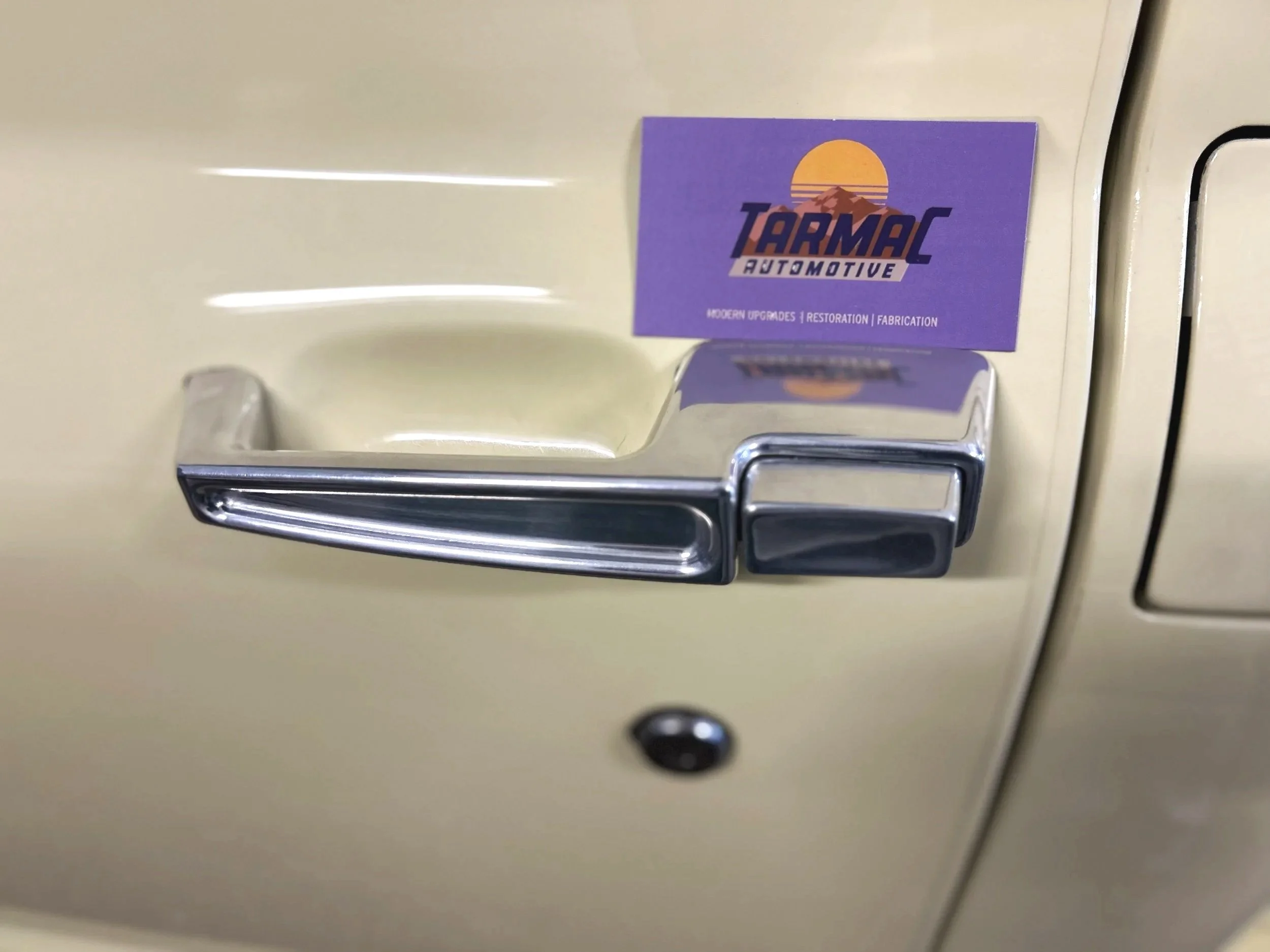 A close-up of a beige vehicle door handle with a purple business card reading "Tarmac Automotive" attached above it.