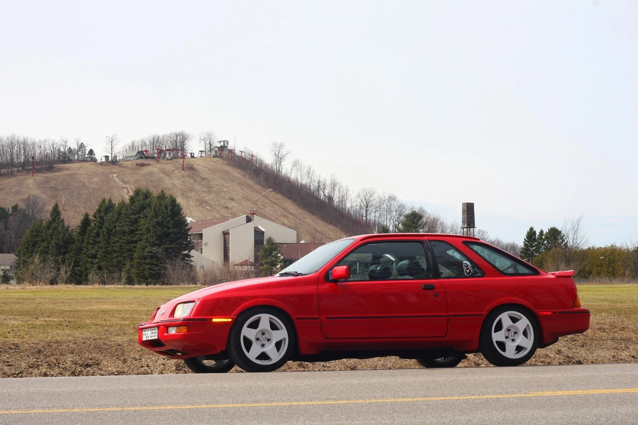 Red sports car parked on side of the road with a hill and trees in the background