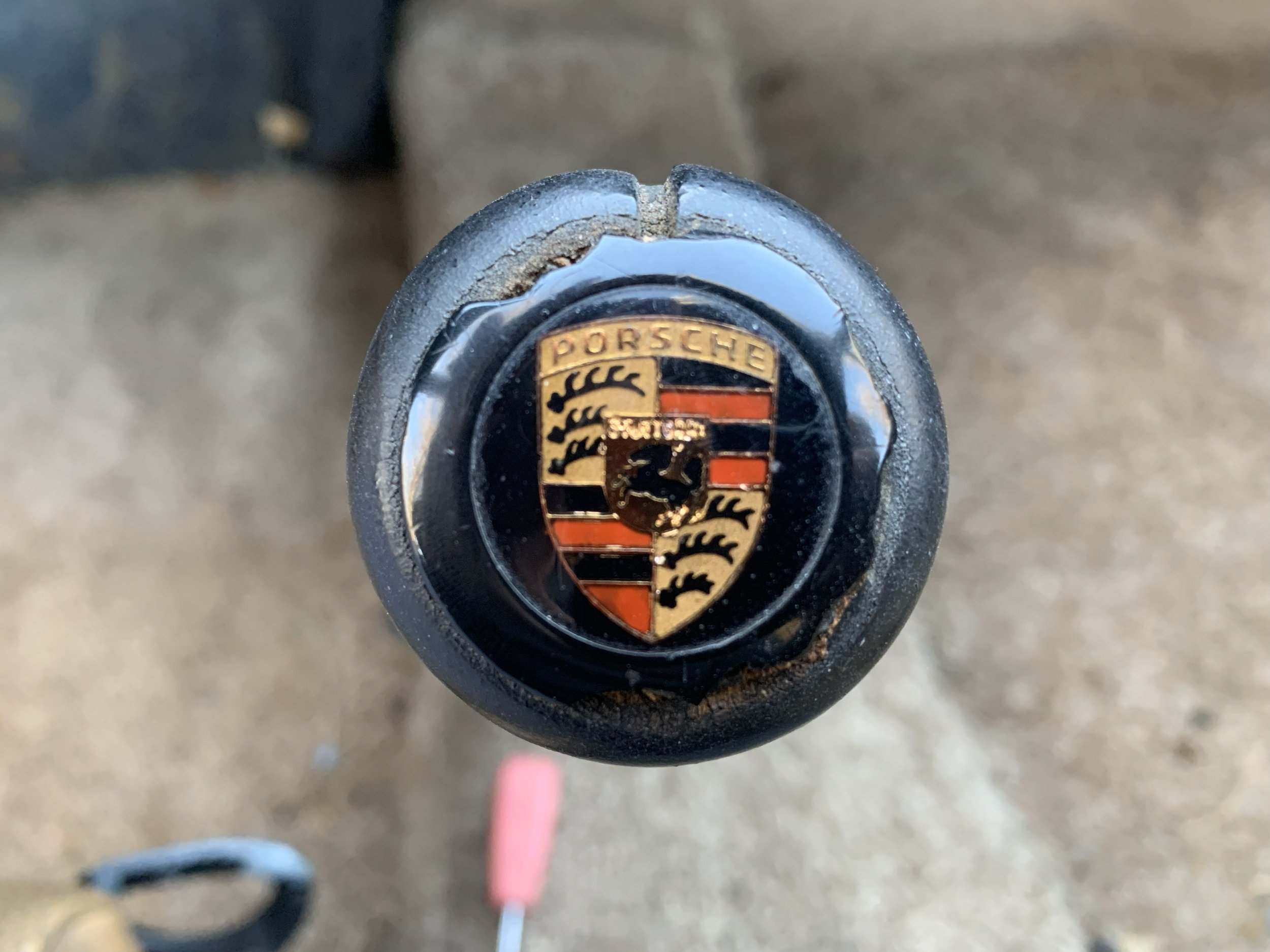 Close-up of a Porsche steering wheel logo on a vehicle steering wheel, showing the black and gold crest with the Porsche name at the top.