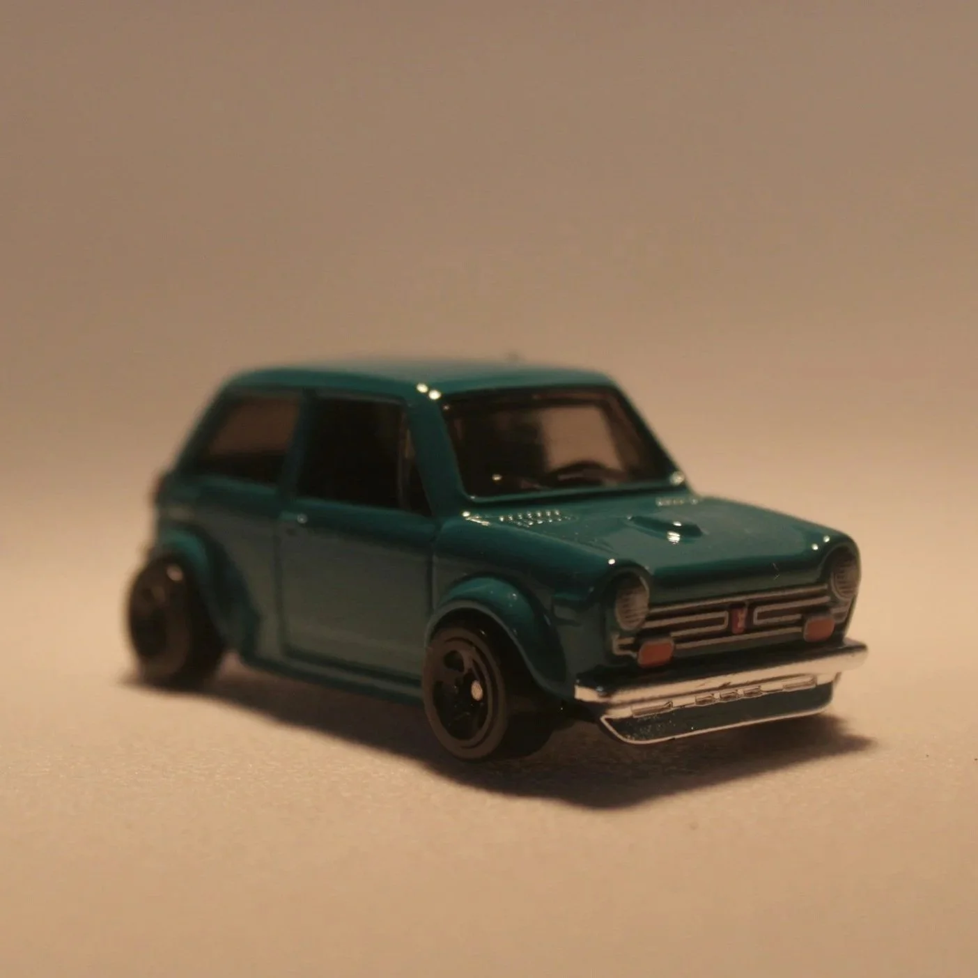 Small teal diecast model car with black wheels on a beige surface.