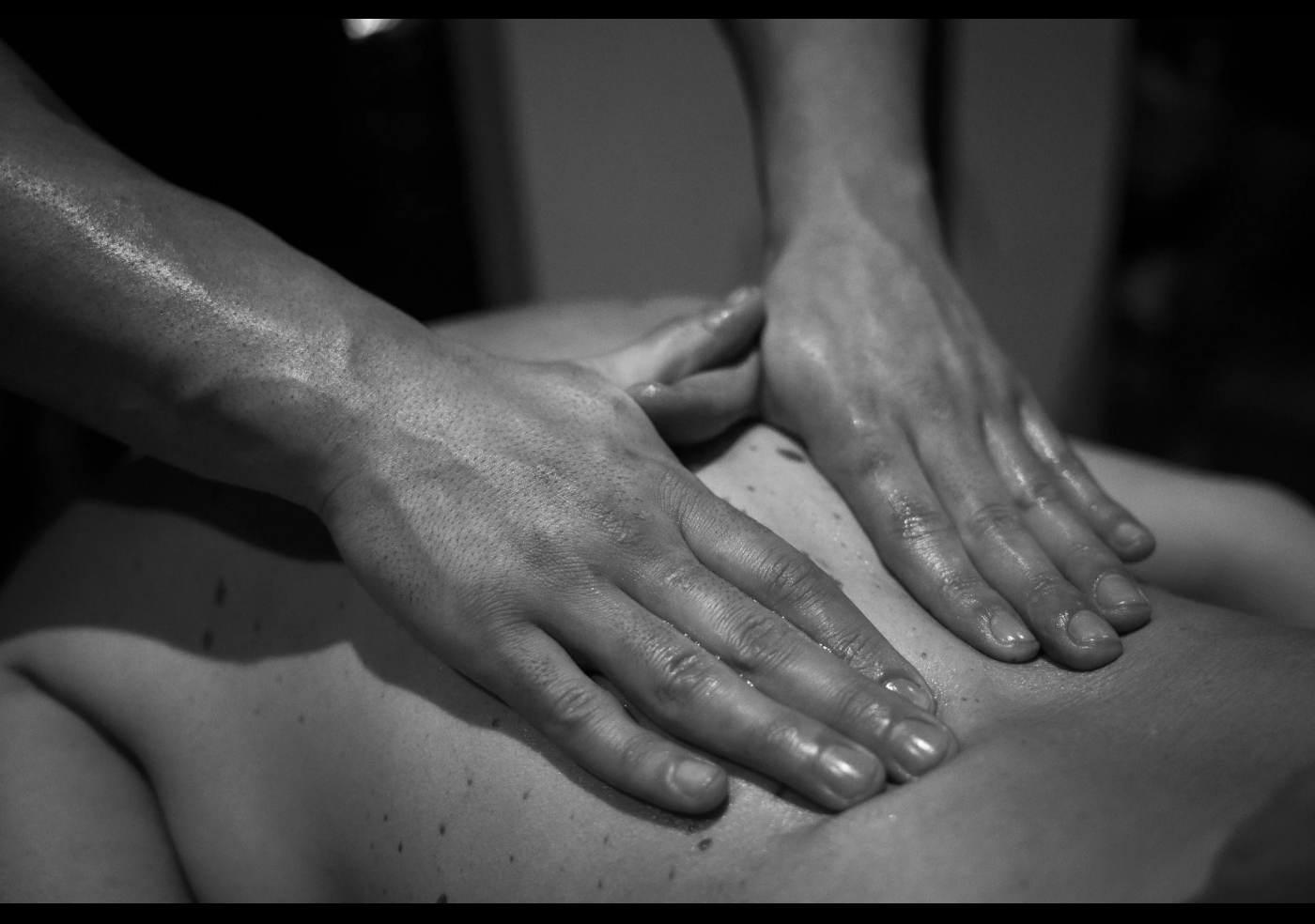 Black and white photo of a person giving a massage, with hands pressing on another person's back.
