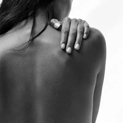 Close-up of a person's shoulder and back with their hand resting on their shoulder, in black and white.