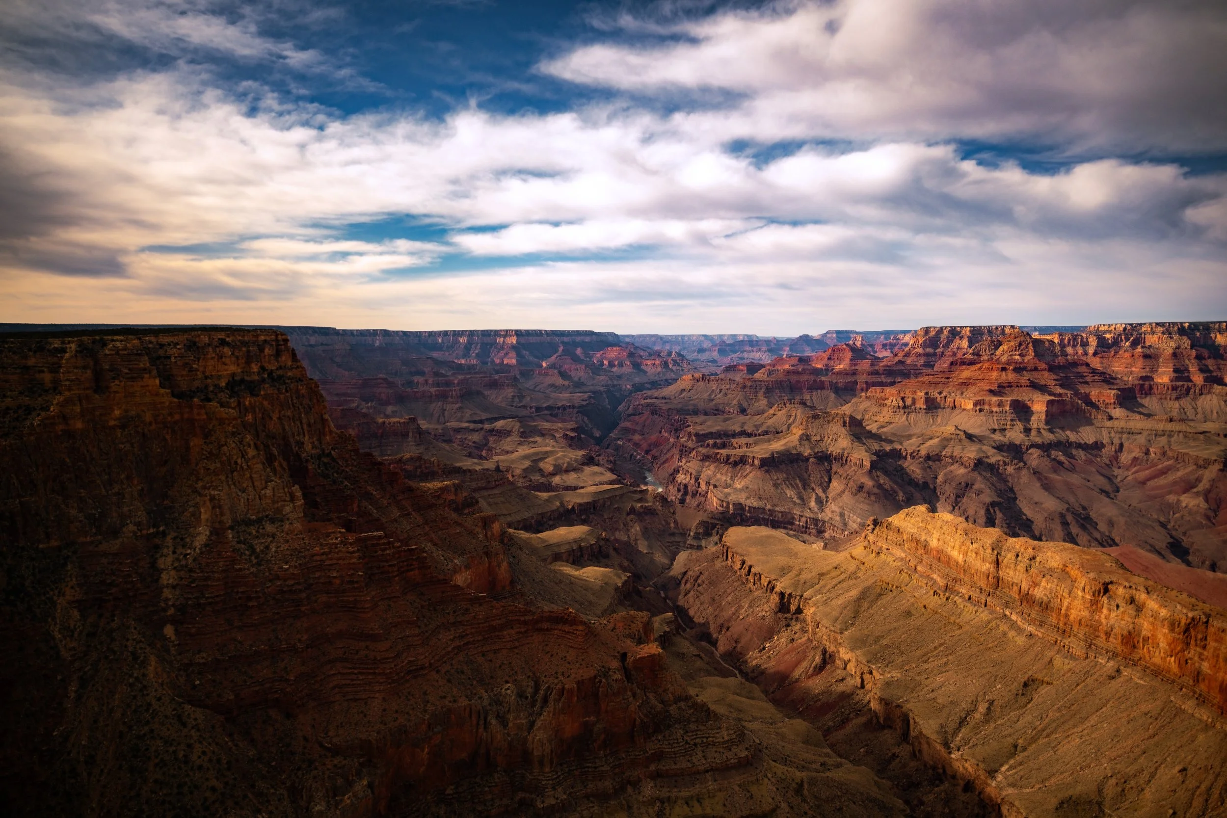 A view of the Grand Canyon with layered red rocks and a cloudy sky.