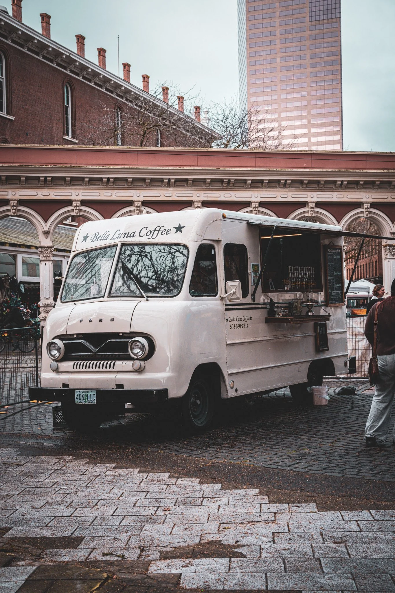 A white food truck with the words 'Bella Luna Coffee' on the front, parked on a cobblestone street with buildings and trees in the background.