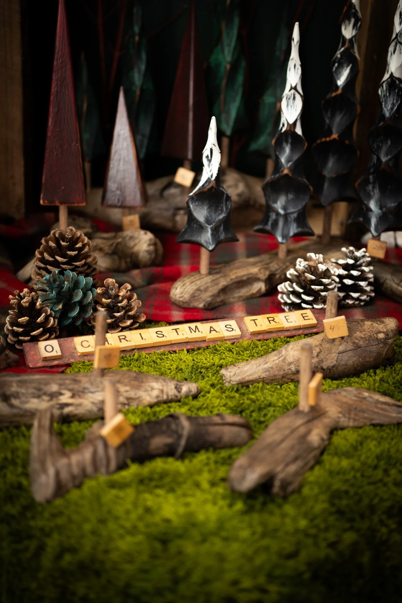 Decorative Christmas display with wooden trees, pinecones, moss, and Scrabble tiles spelling 'O CHRISTMAS TREE' on a rustic wood and moss surface.